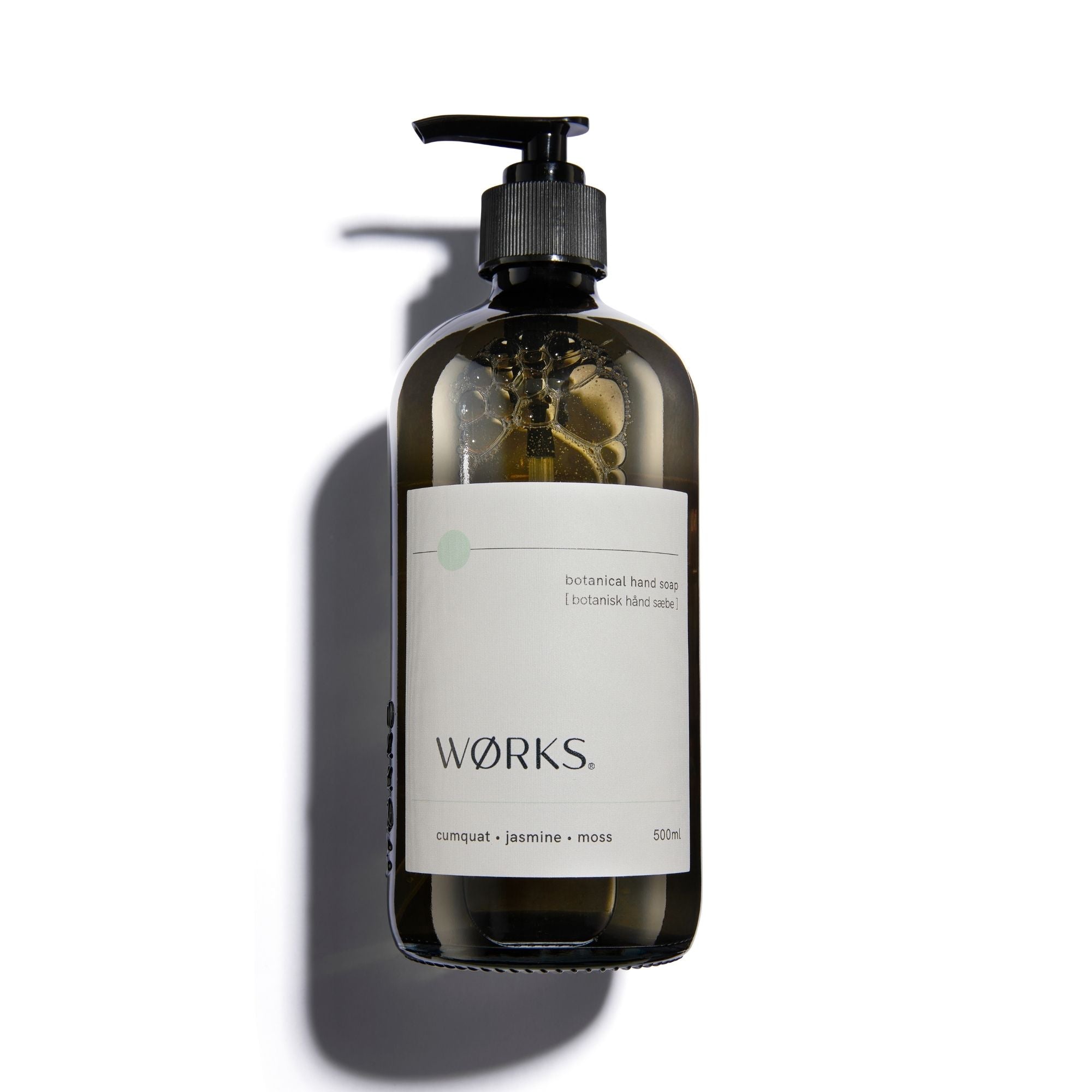 A brown glass hand soap bottle with a black pump and label with 'Works' branding.