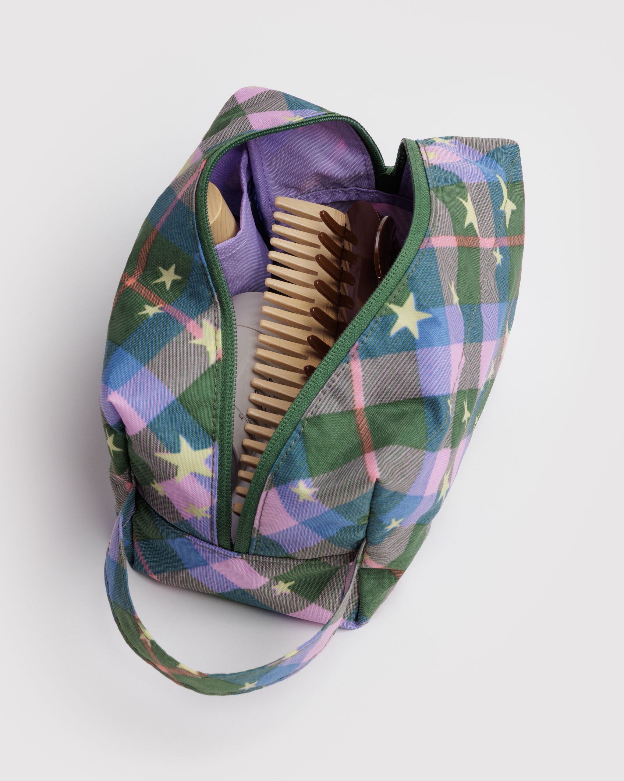 Green zip open on green plaid and stars patterned bag with purple lining and side pouches storing toiletries inside and hanging or carrying loop at end.
