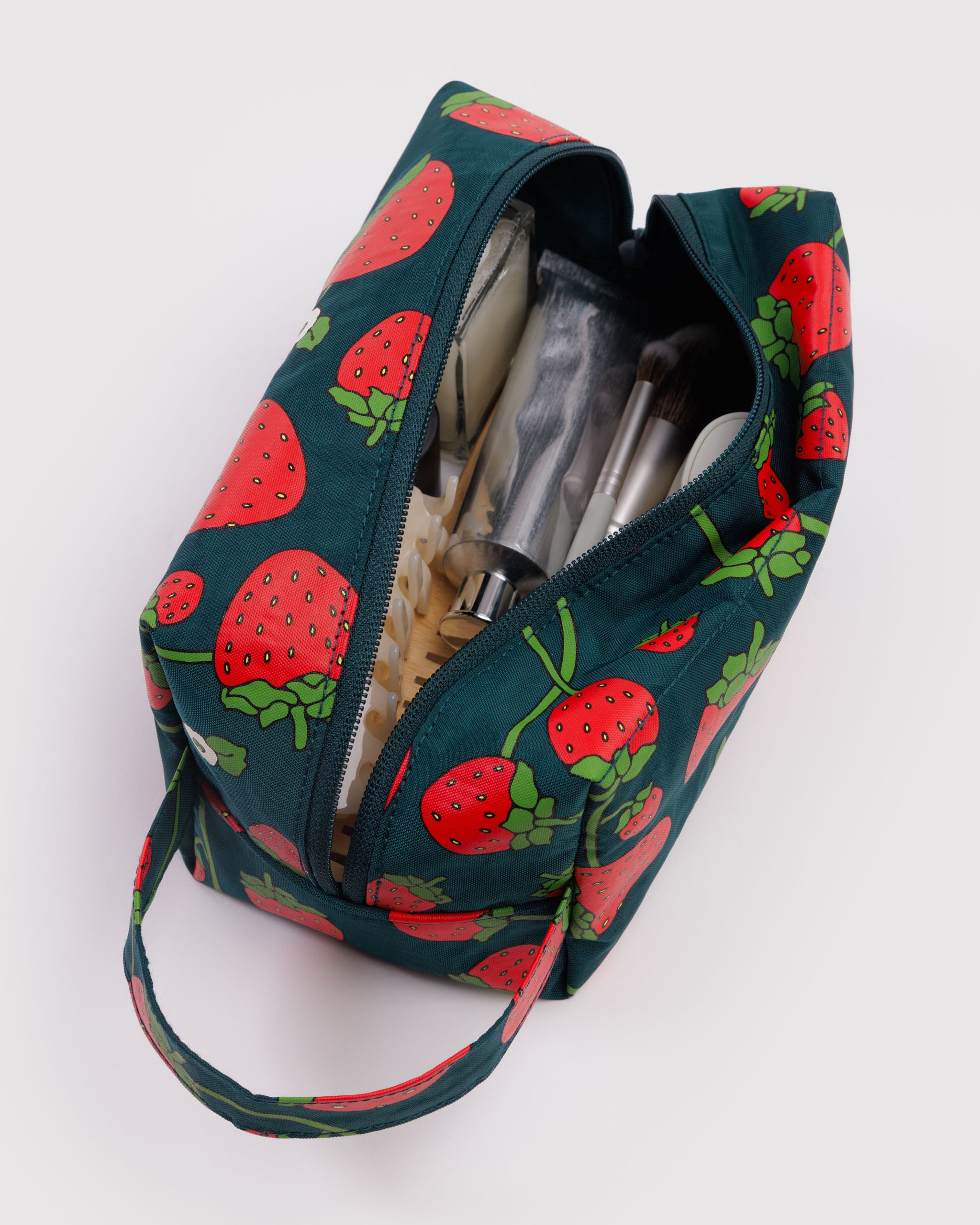 Strawberry-patterned bag sitting flat on bottom with zip open and cosmetics inside.