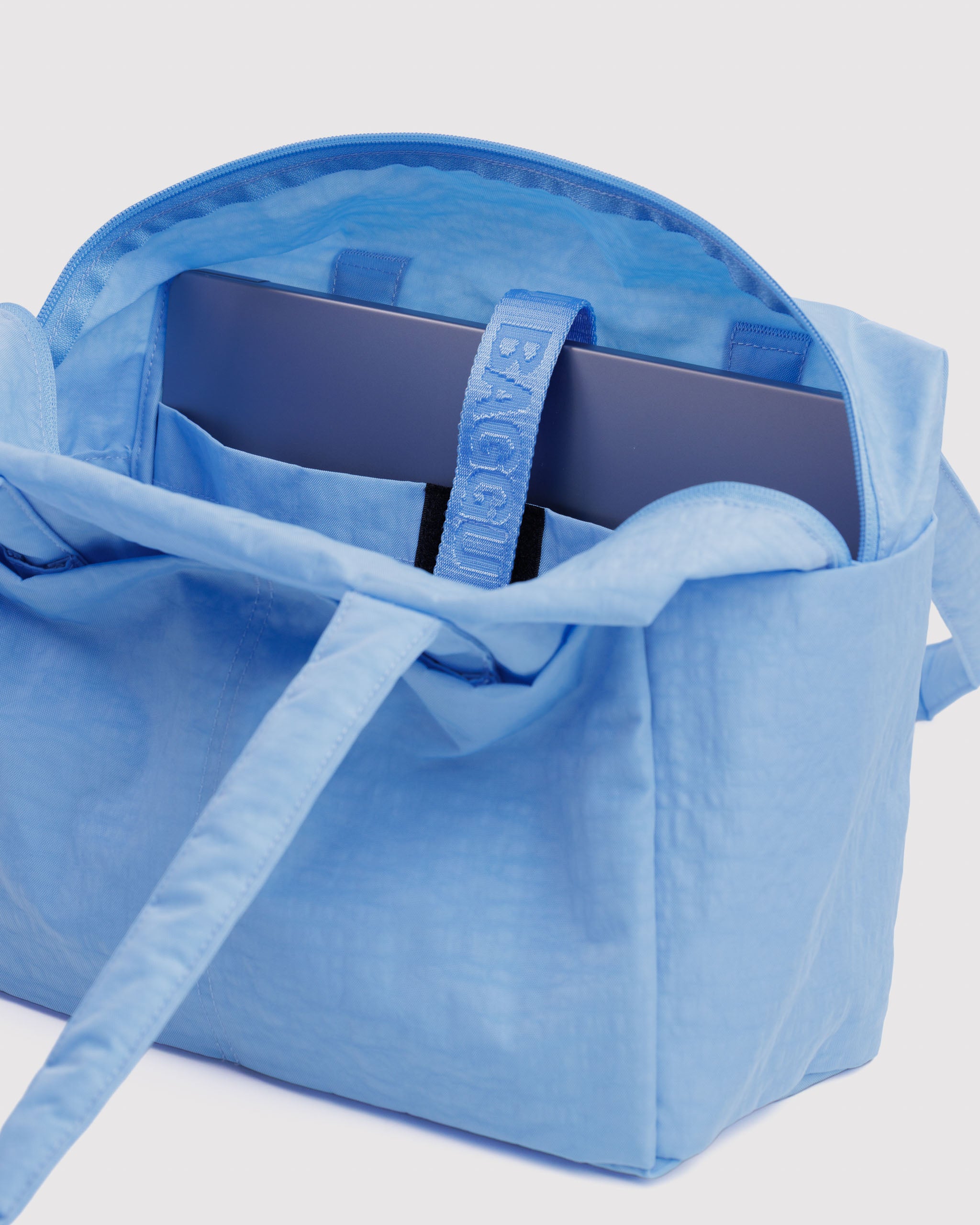 Blue tote bag with a laptop inside in a pocket with velcro closure.