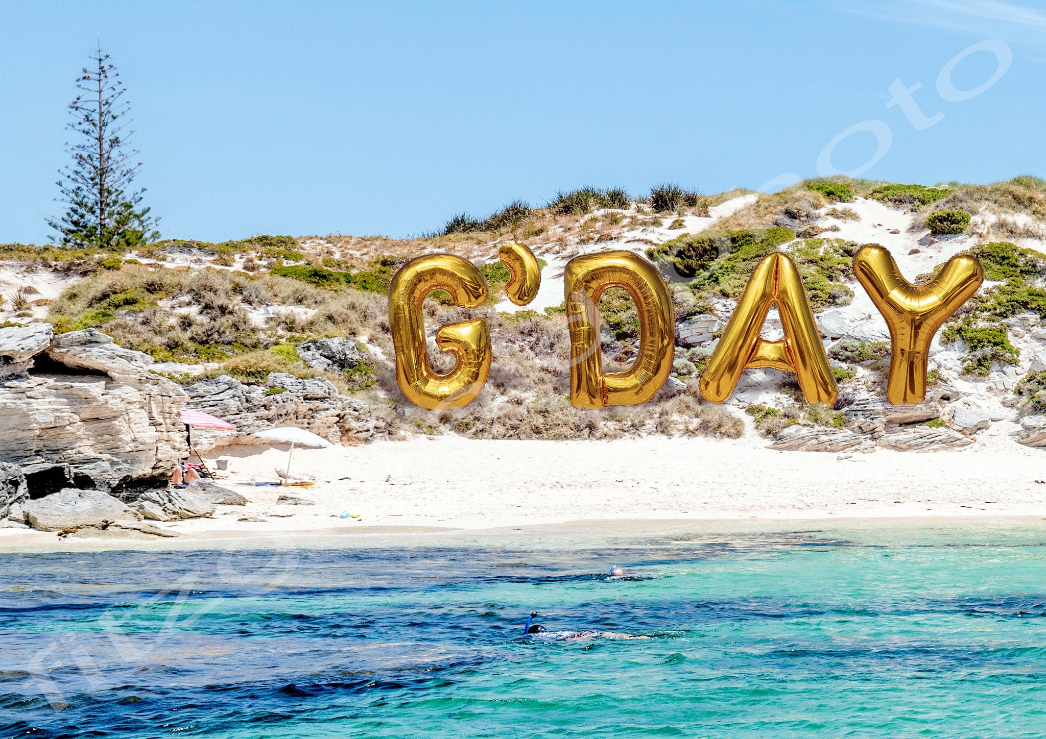 Beach scene with gold balloons spelling 'G'DAY' on sand dune.