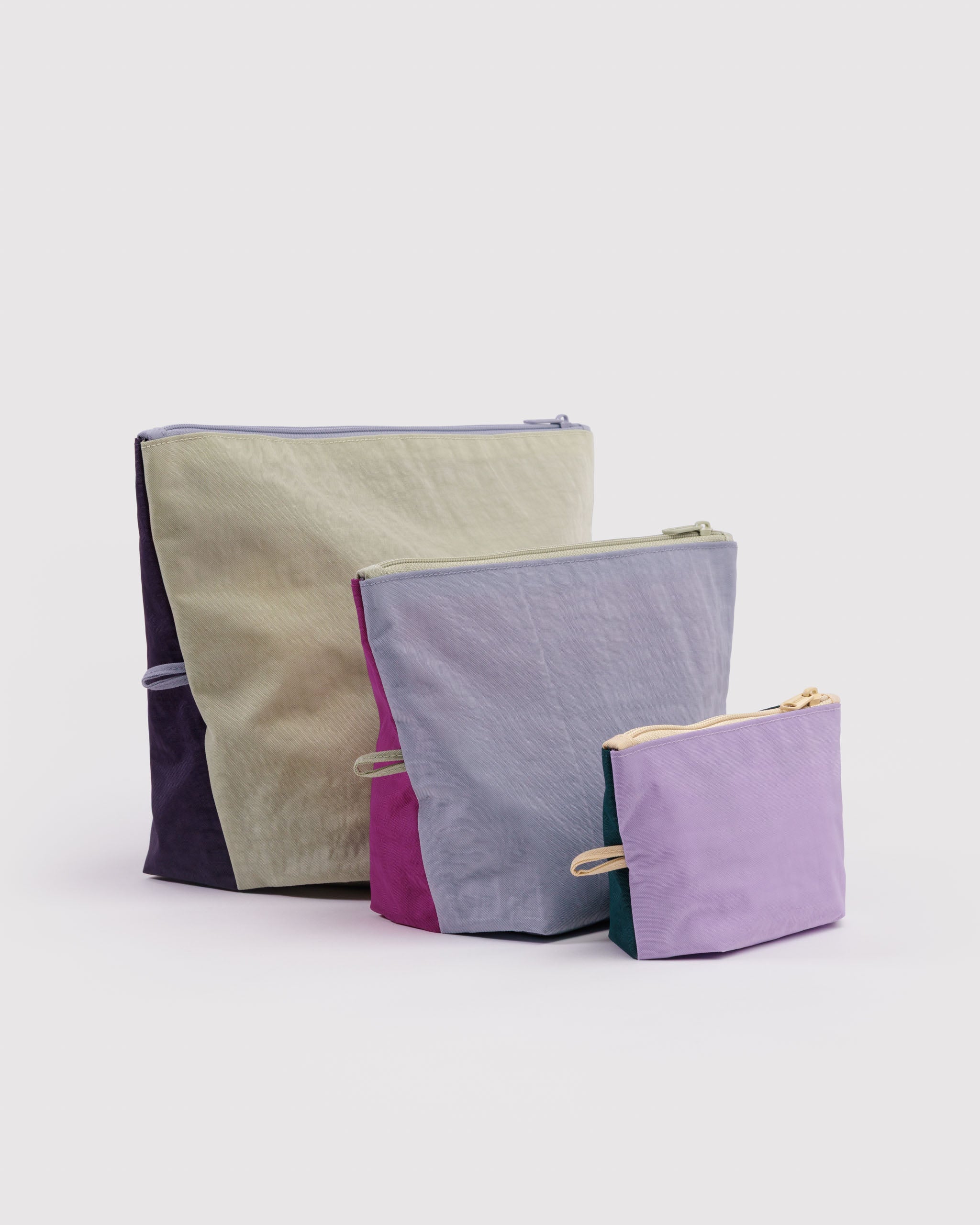 Three different sized and pastel coloured expanded zip top pouches with items inside, hanging loop and standing upright on flat bottom.