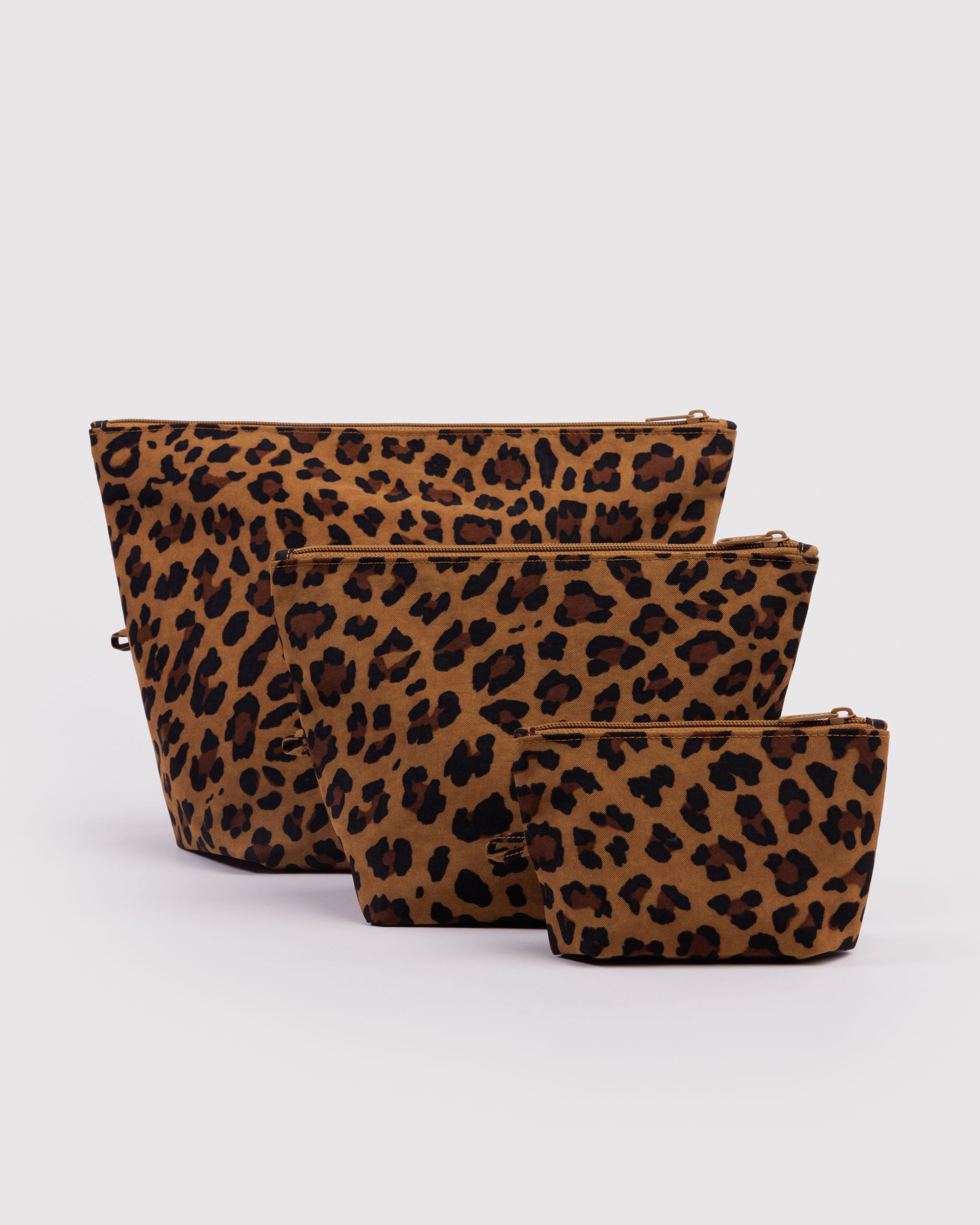 Three different sized and leopard print expanded zip top pouches with items inside, hanging loop and standing upright on flat bottom.