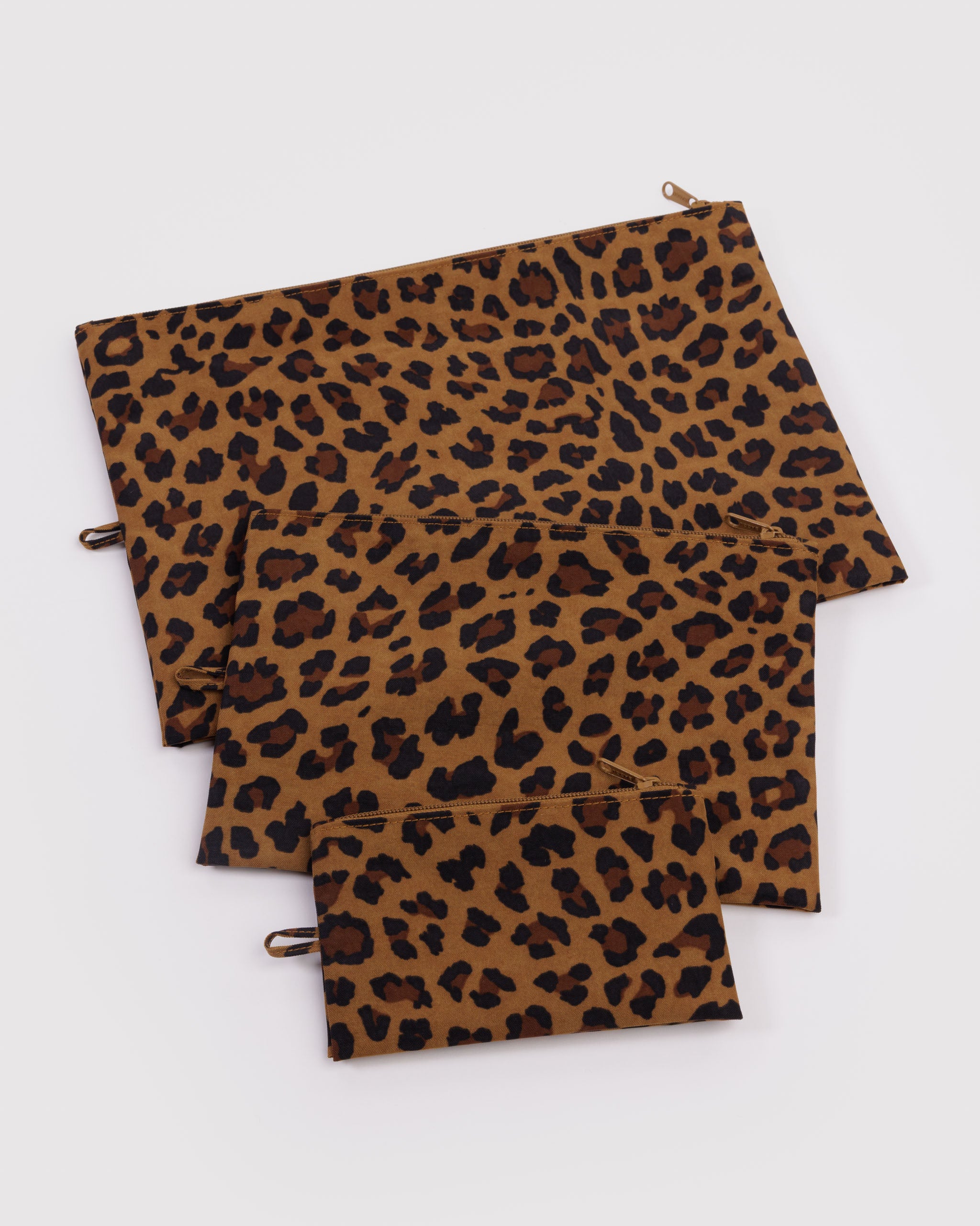 Three different sized leopard print zip top pouches with hanging loop at side lying empty and flat.