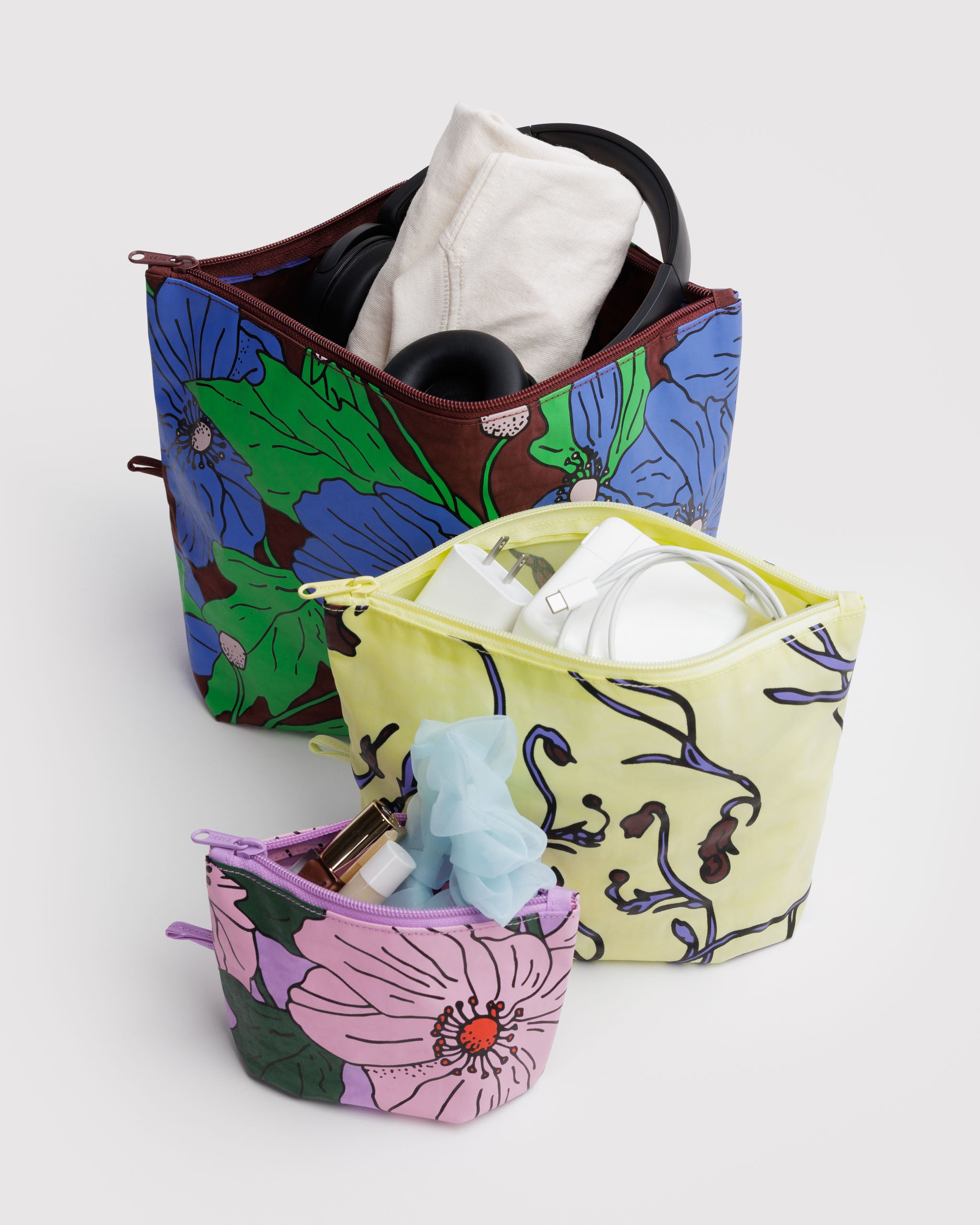 Three floral-patterned pouches with zip top open containing various items, tech cords, cosmetics, headphones.