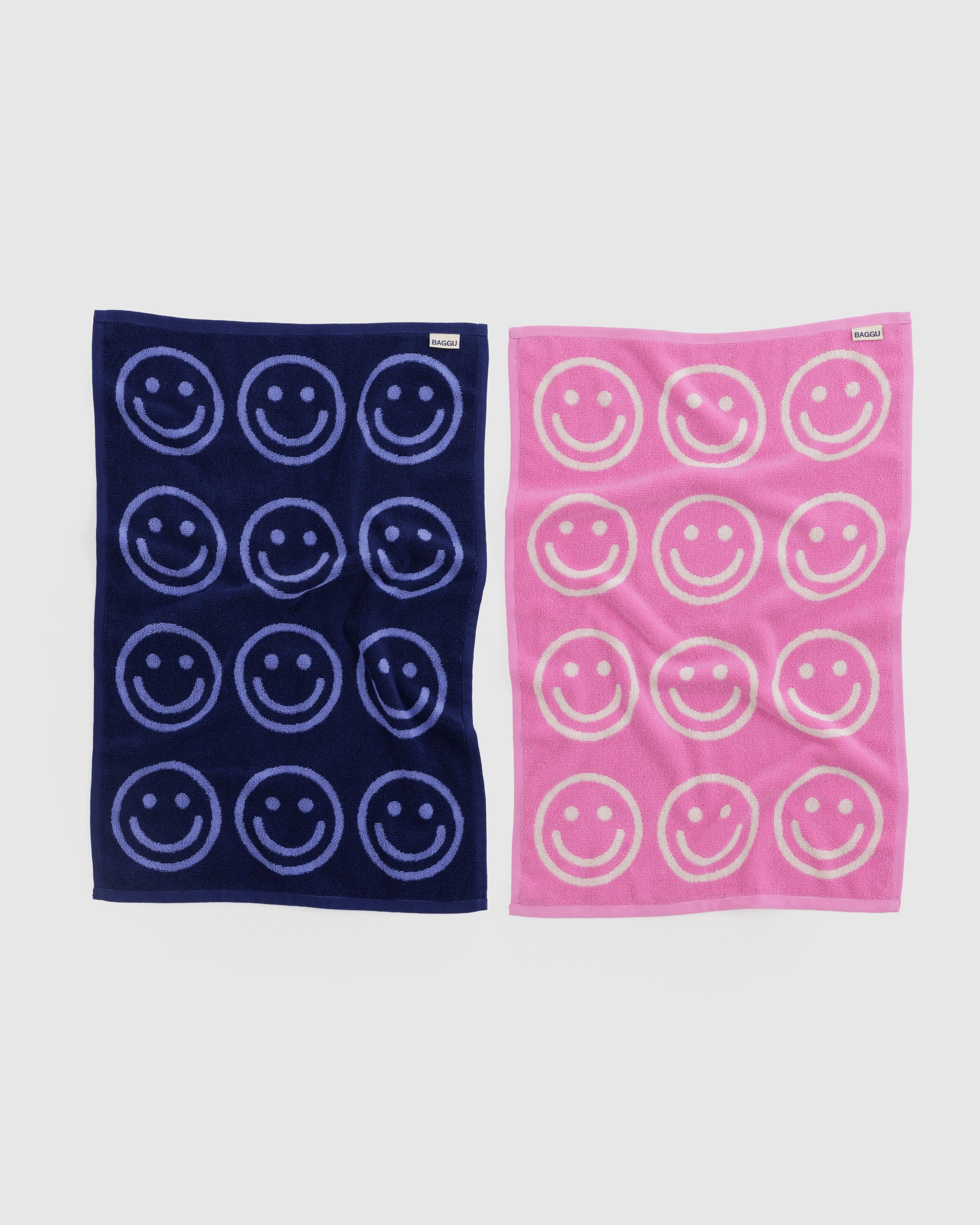 Two hand towels, one navy with smiley face patterns and one pink with white smiley faces, and a BAGGU label.