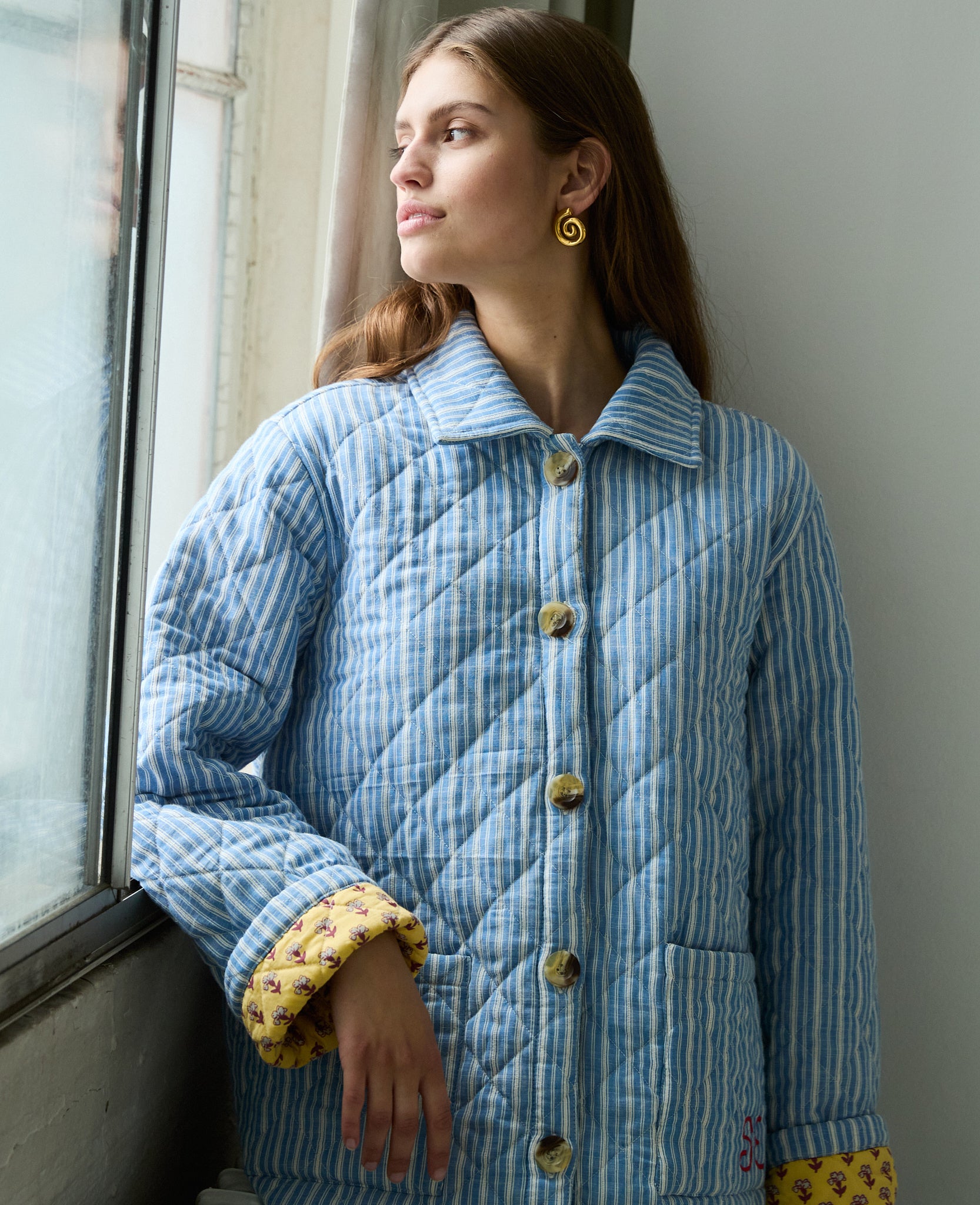 woman-wearing-blue-and-white-striped-quilted-jacket-with-collar-and-yellow-floral-lining-buttons-done-up-two-patch-pockets