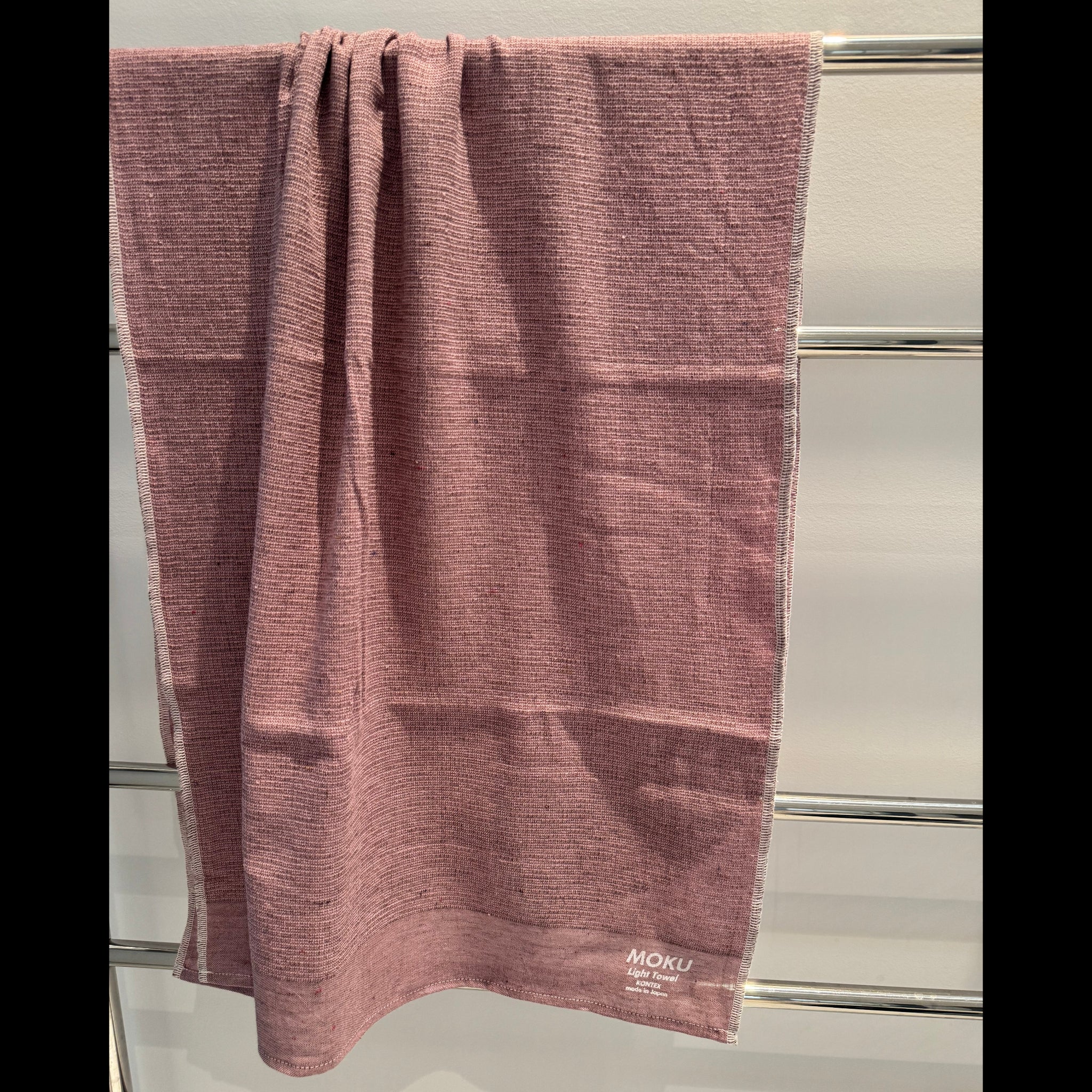 Pink bath towel with 'MOKU' branding hanging on a towel rail.