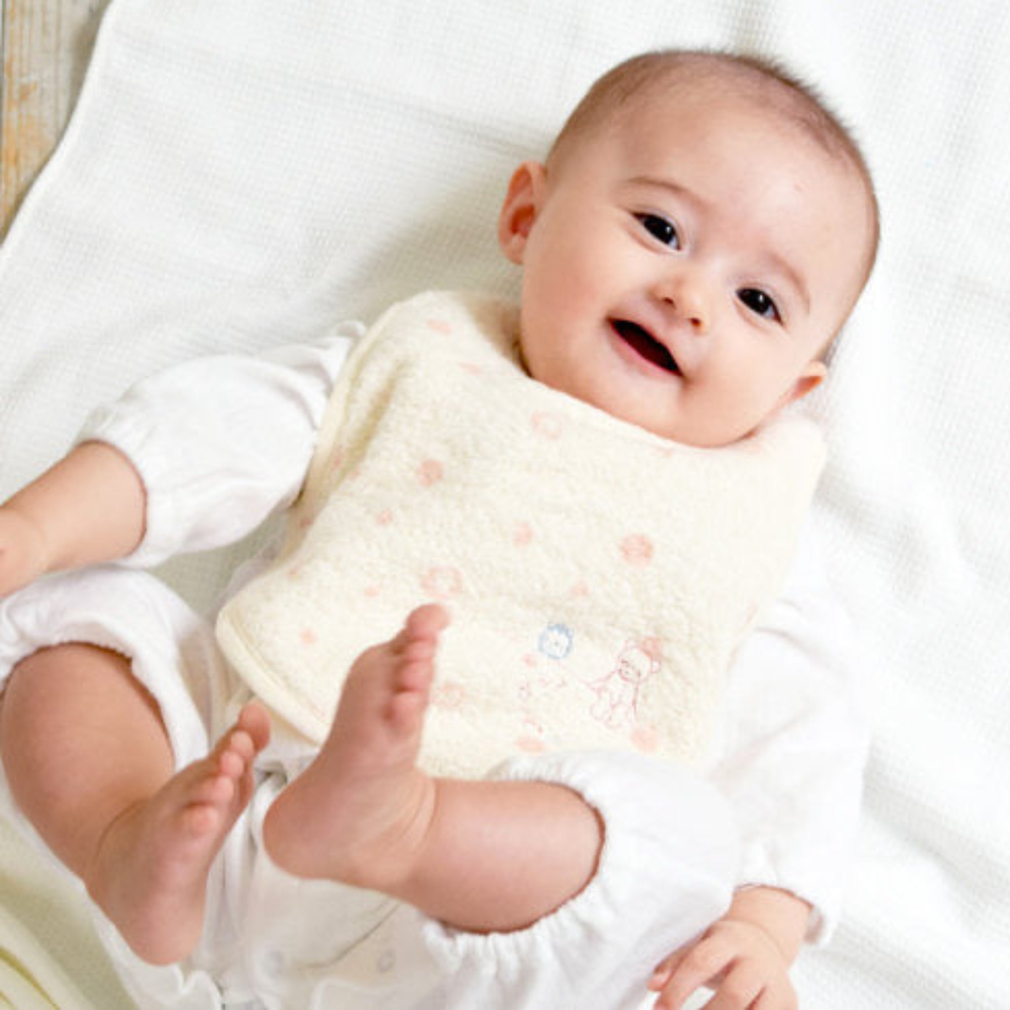 Baby wearing a cream bib with peach pink polka dots and embroidered  teddy.