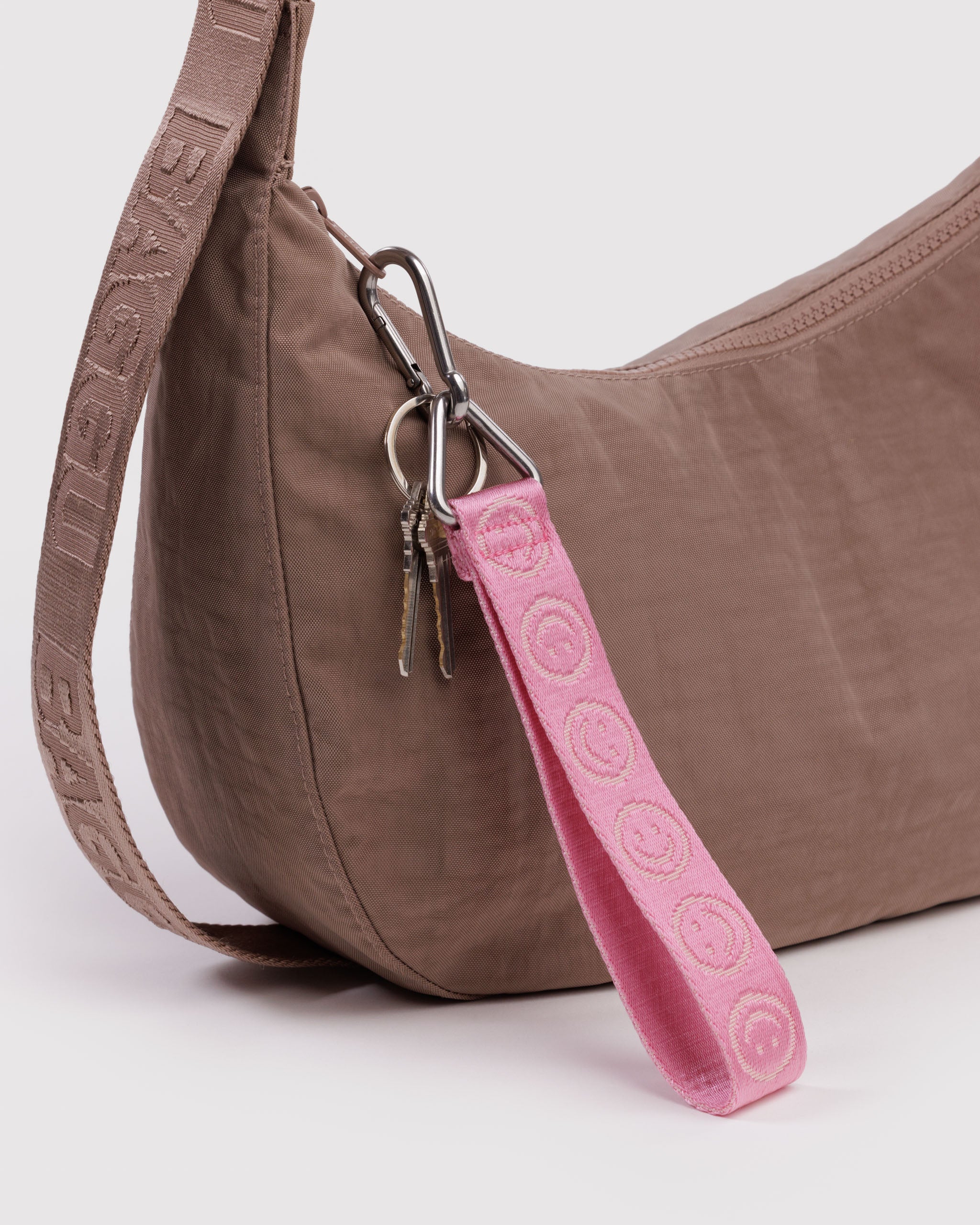 Brown handbag with a pink keychain strap with smiley face prints and metal triangular ring and clip with keys attached to zip.