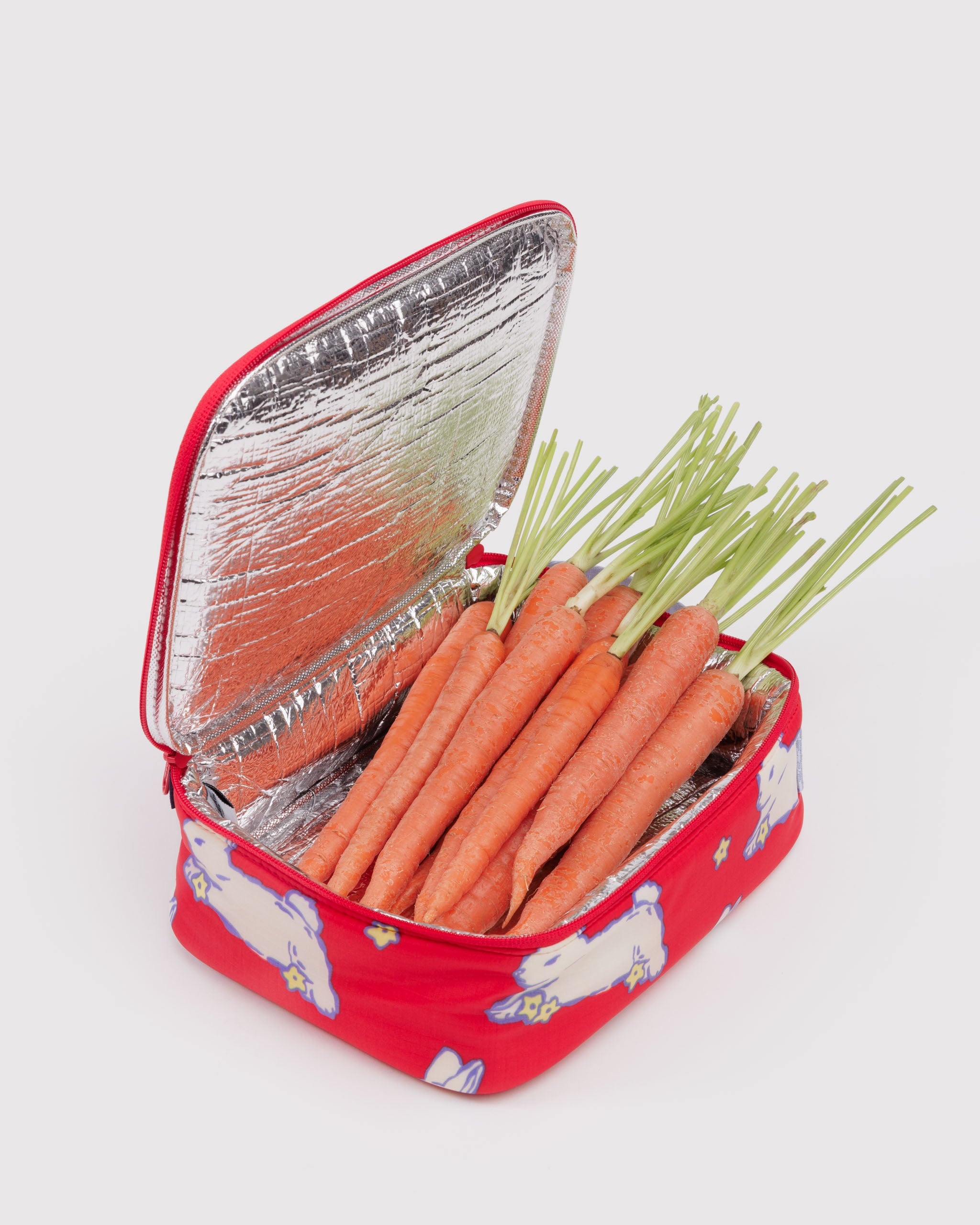 Small insulated lunch box with white bunnies design filled with carrots with green tops.
