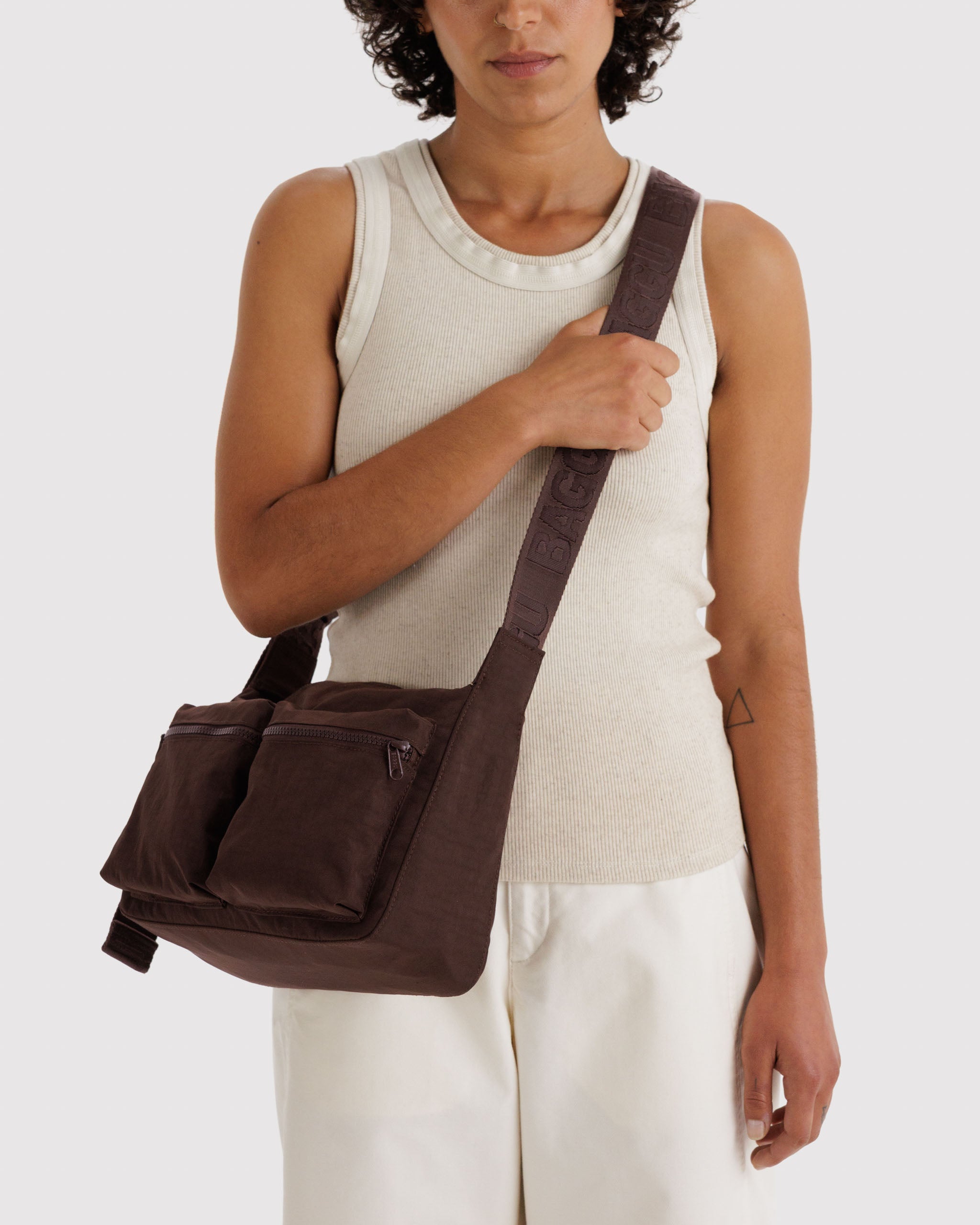 Woman carrying a brown shoulder bag crossbody on shoulder.