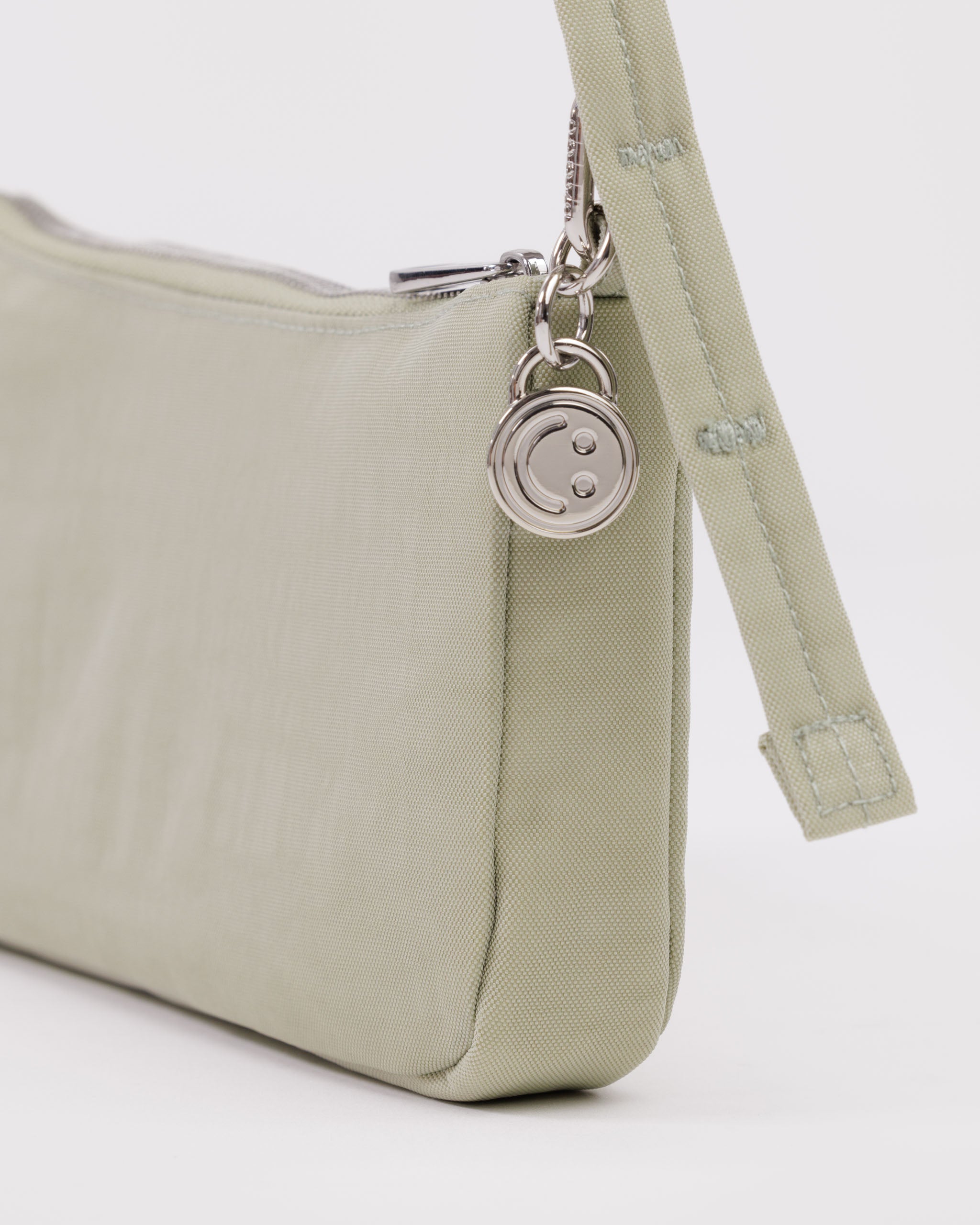 Light green handbag with adjustable strap and metal smiley face charm attached.