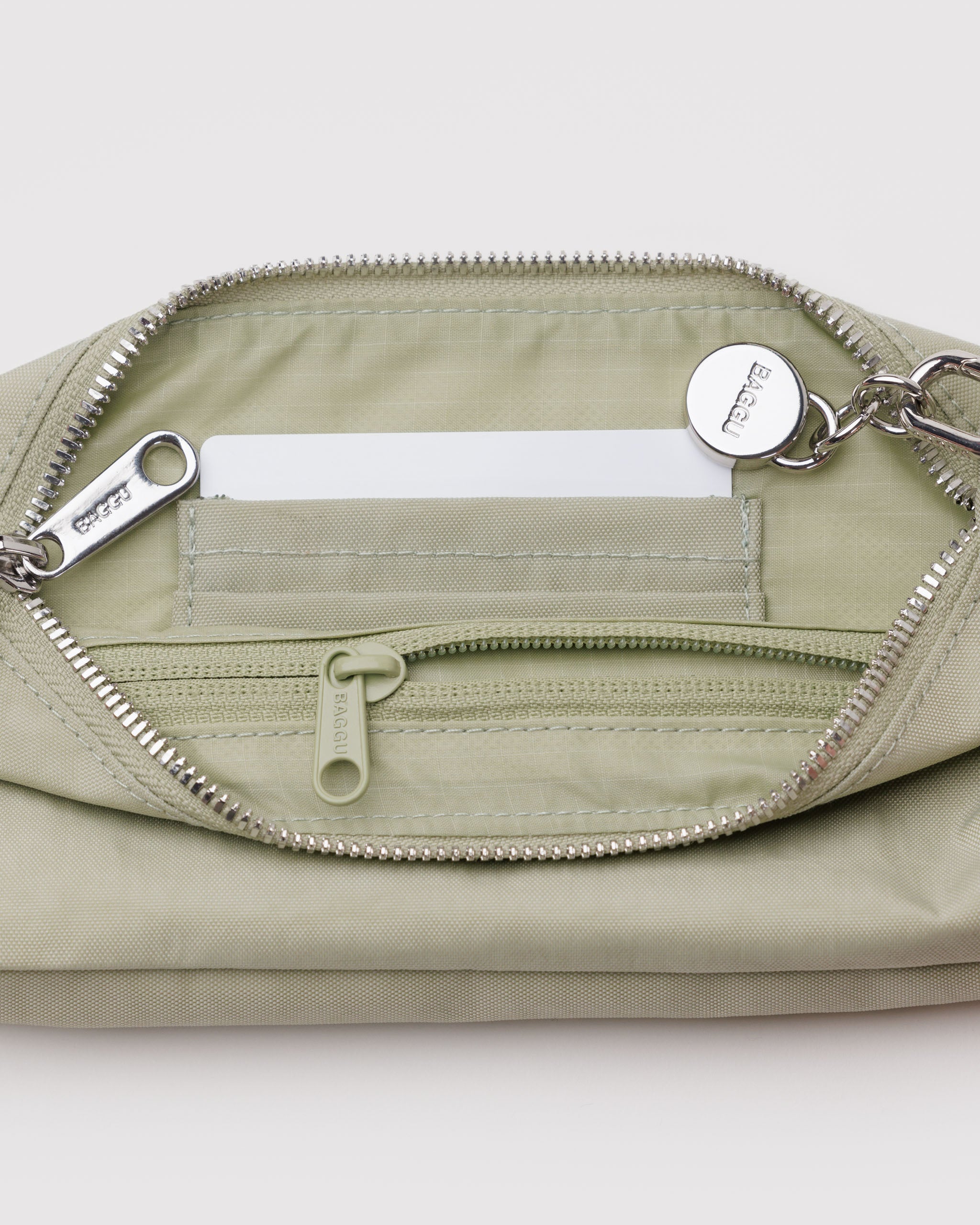 Inside a light green bag with metal top zip closure and a metal BAGGU branded charm attached with a tonal internal zip pocket and card slots.