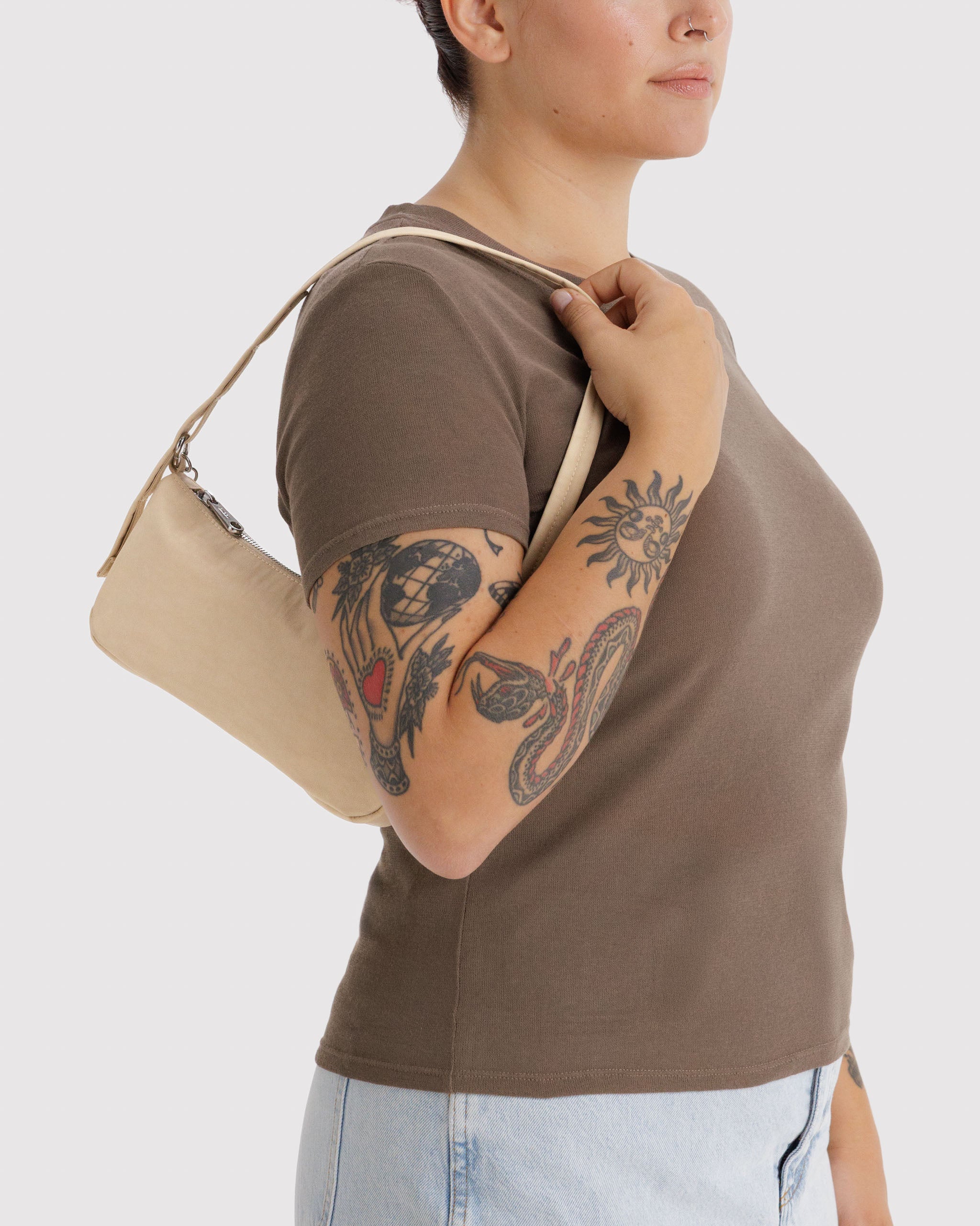 Person wearing a brown shirt holding adjustable strap of a light yellow handbag on shoulder.