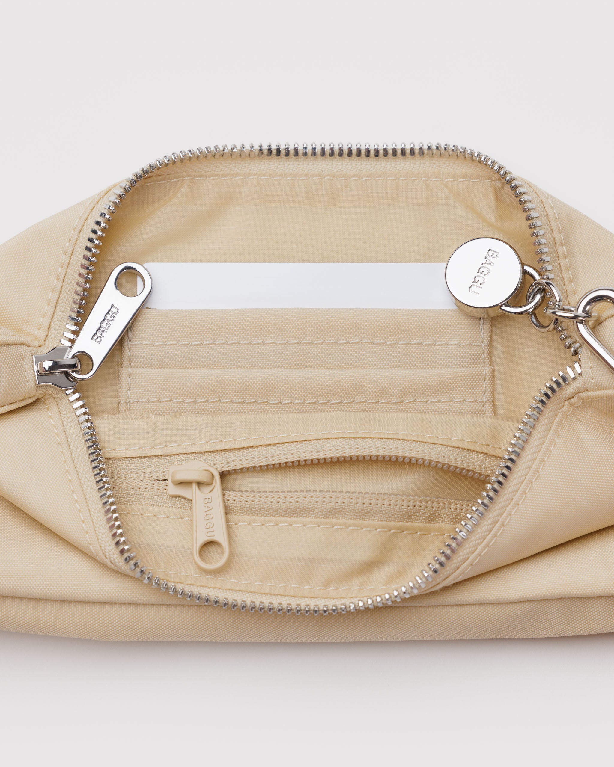 Inside a light yellow handbag with a top metal top zip closure and a metal smiley face charm attached to strap and an internal tonal zip pocket and card slots.