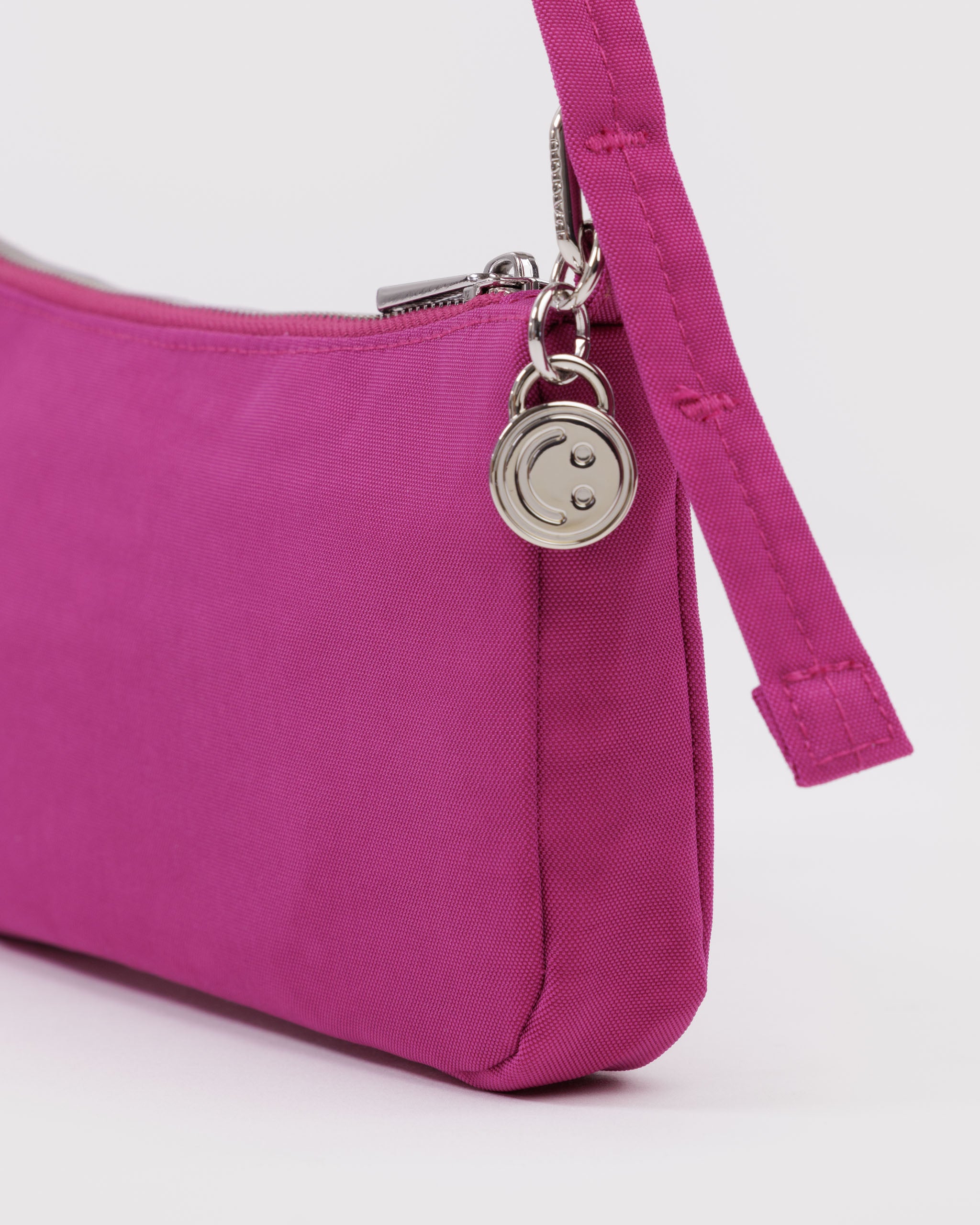 Close-up of a vibrant pink handbag with a silver zipper and metal smiley face charm attached to strap.