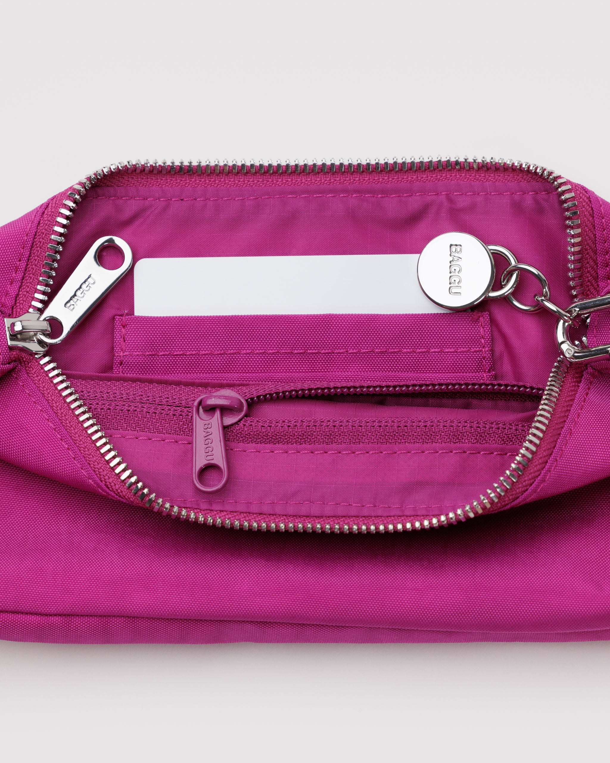 Vibrant pink bag with top zip closure and a zip internal pocket and card slots with a metal smiley face charm attached to strap.