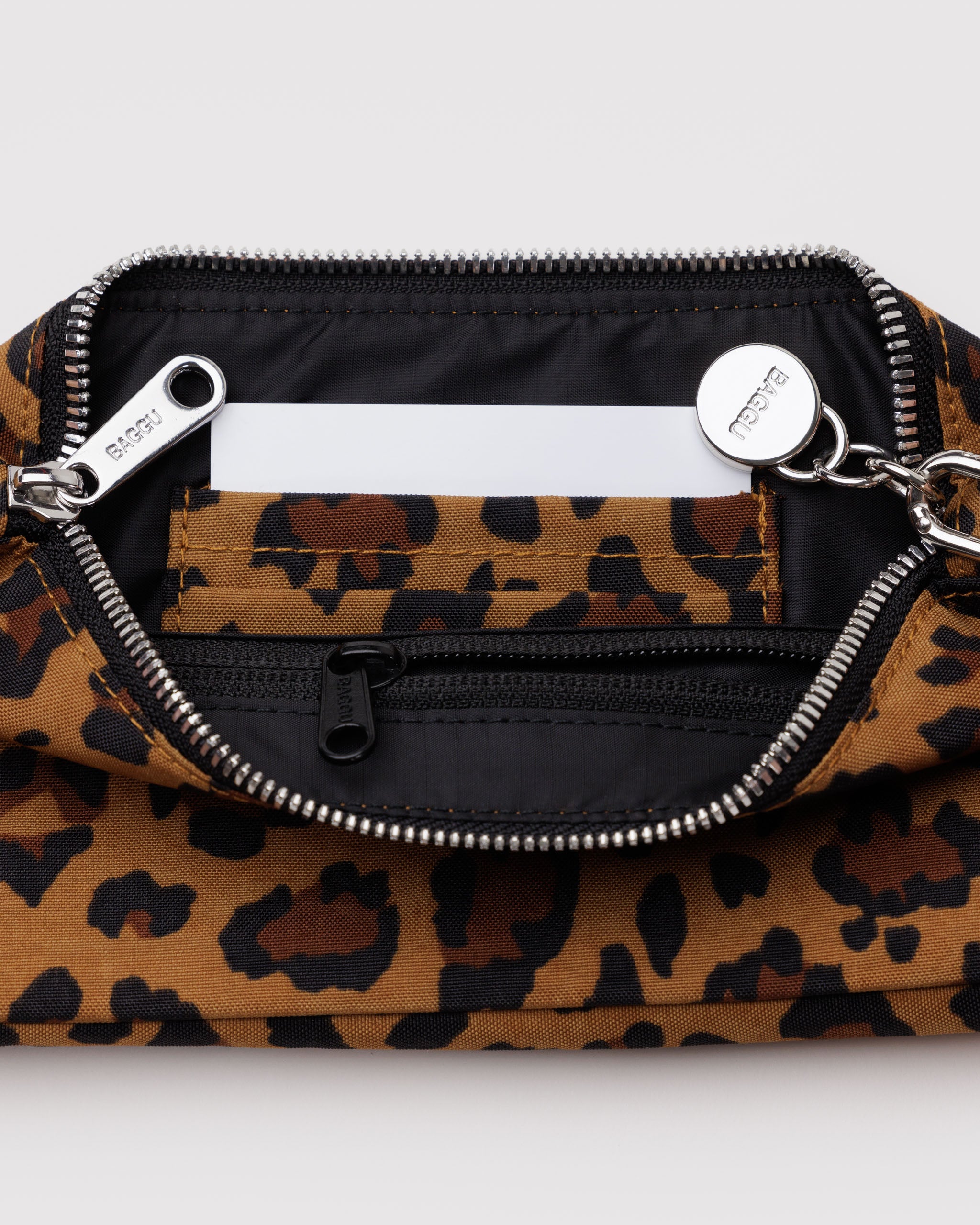 Top metal zip open on a leopard handbag showing internal black zip pocket, leopard print card slots and BAGGU branded metal charm on metal clasp.