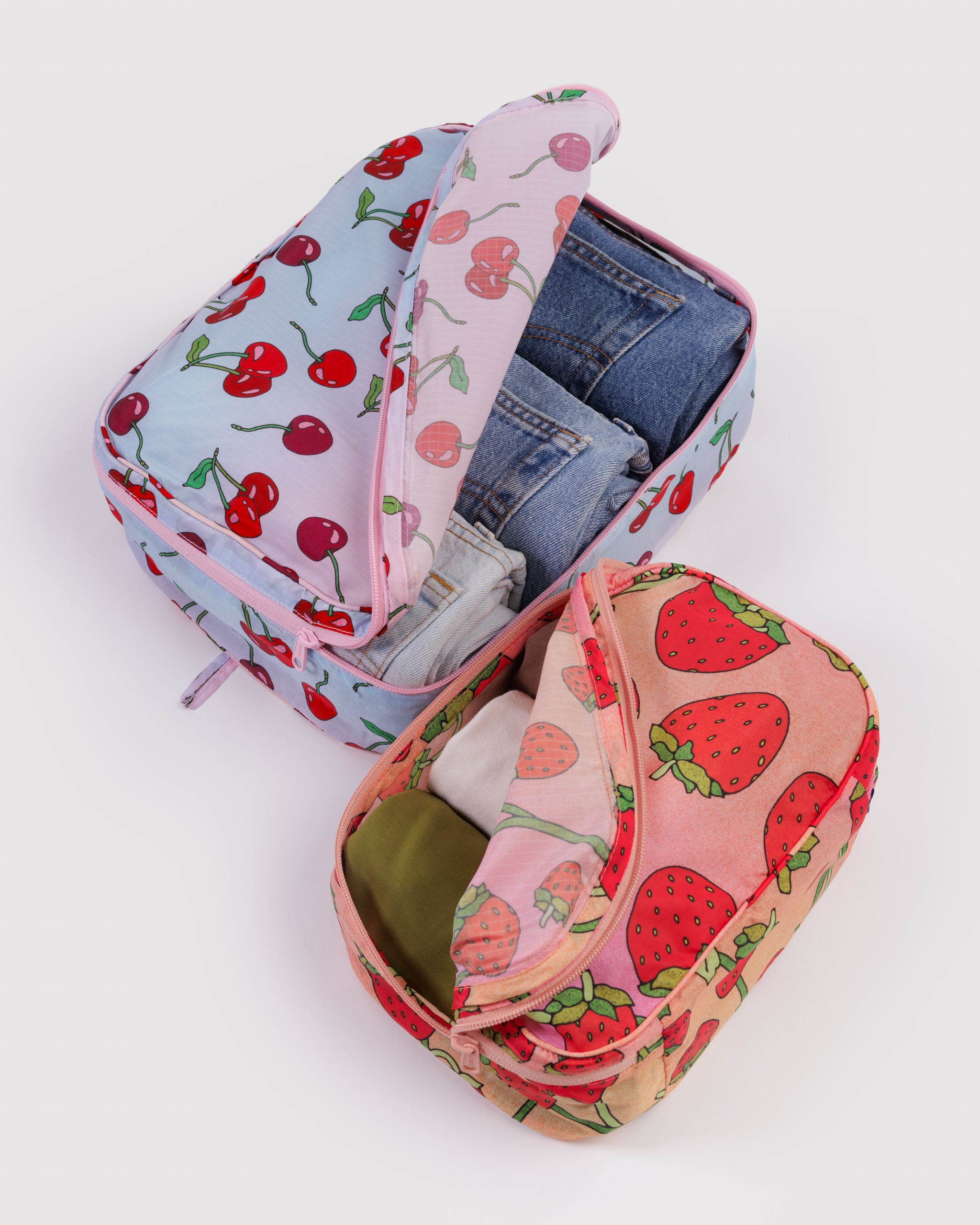 Two zippered packing cubes, a small and a medium size, with cherry and strawberry patterns filled with clothing items.