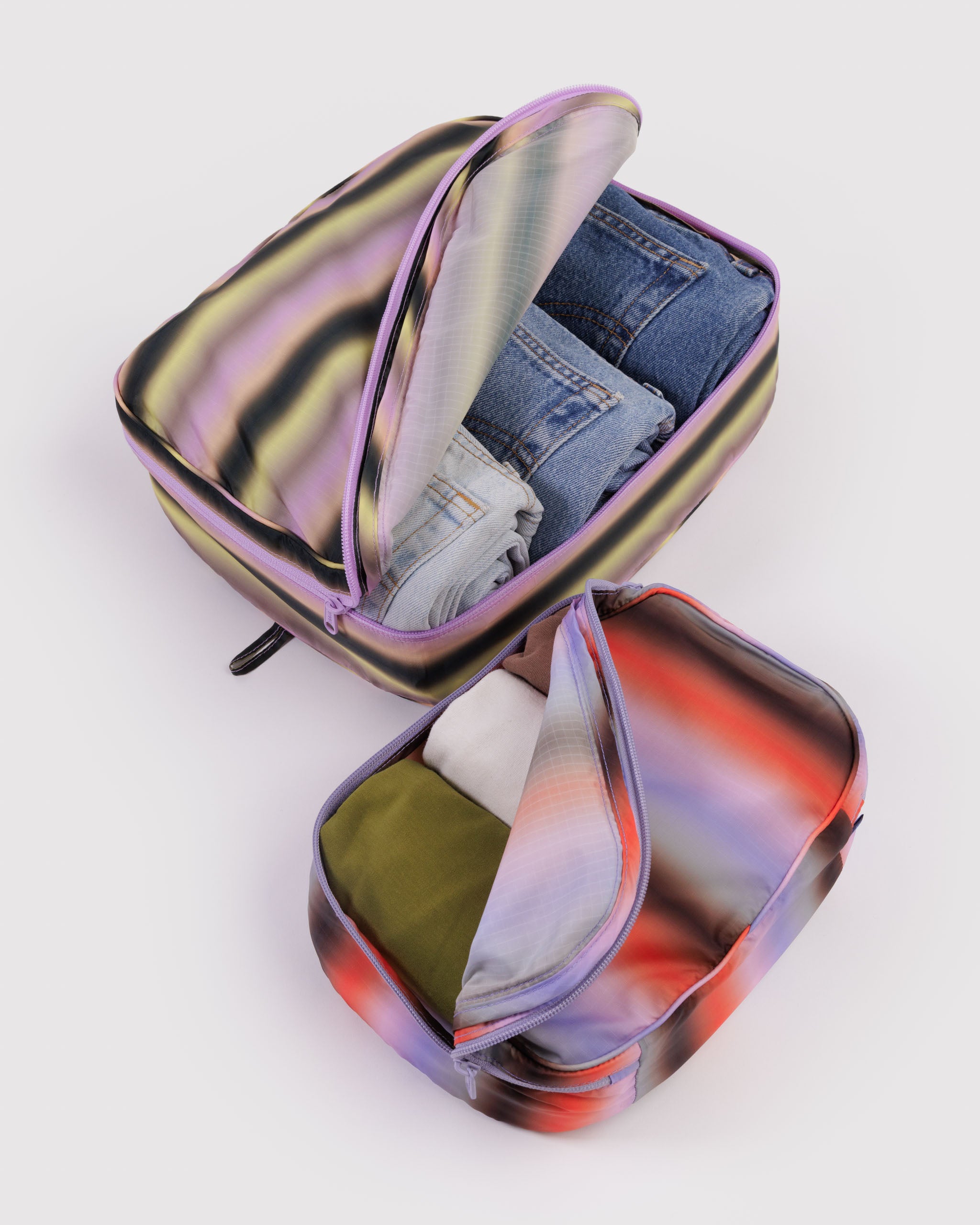 Set of 2 multicoloured packing cubes filled with clothing and zipper half open and flap folded back.