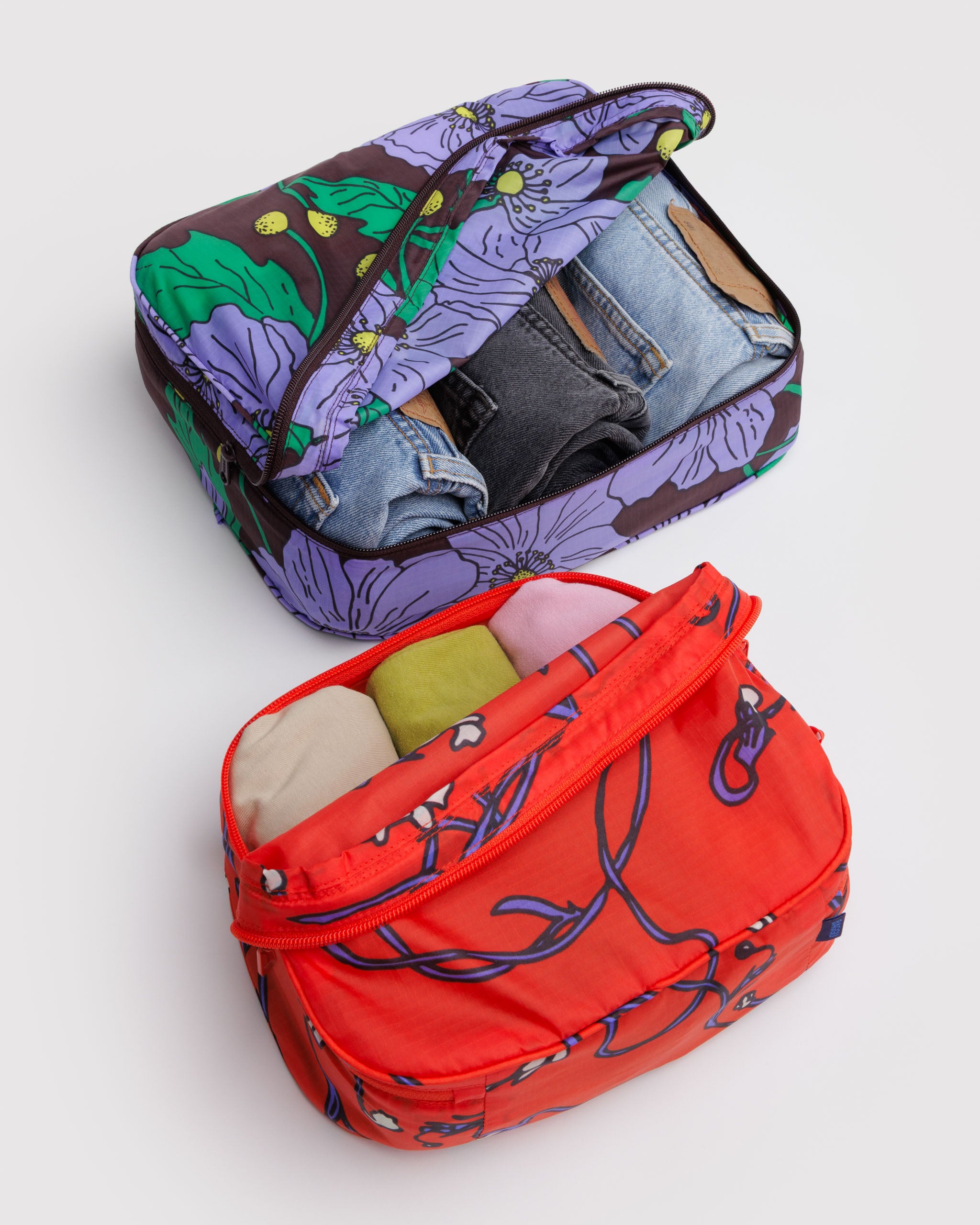 Two floral-patterned packing cubes, one purple and one red, packed with clothing.