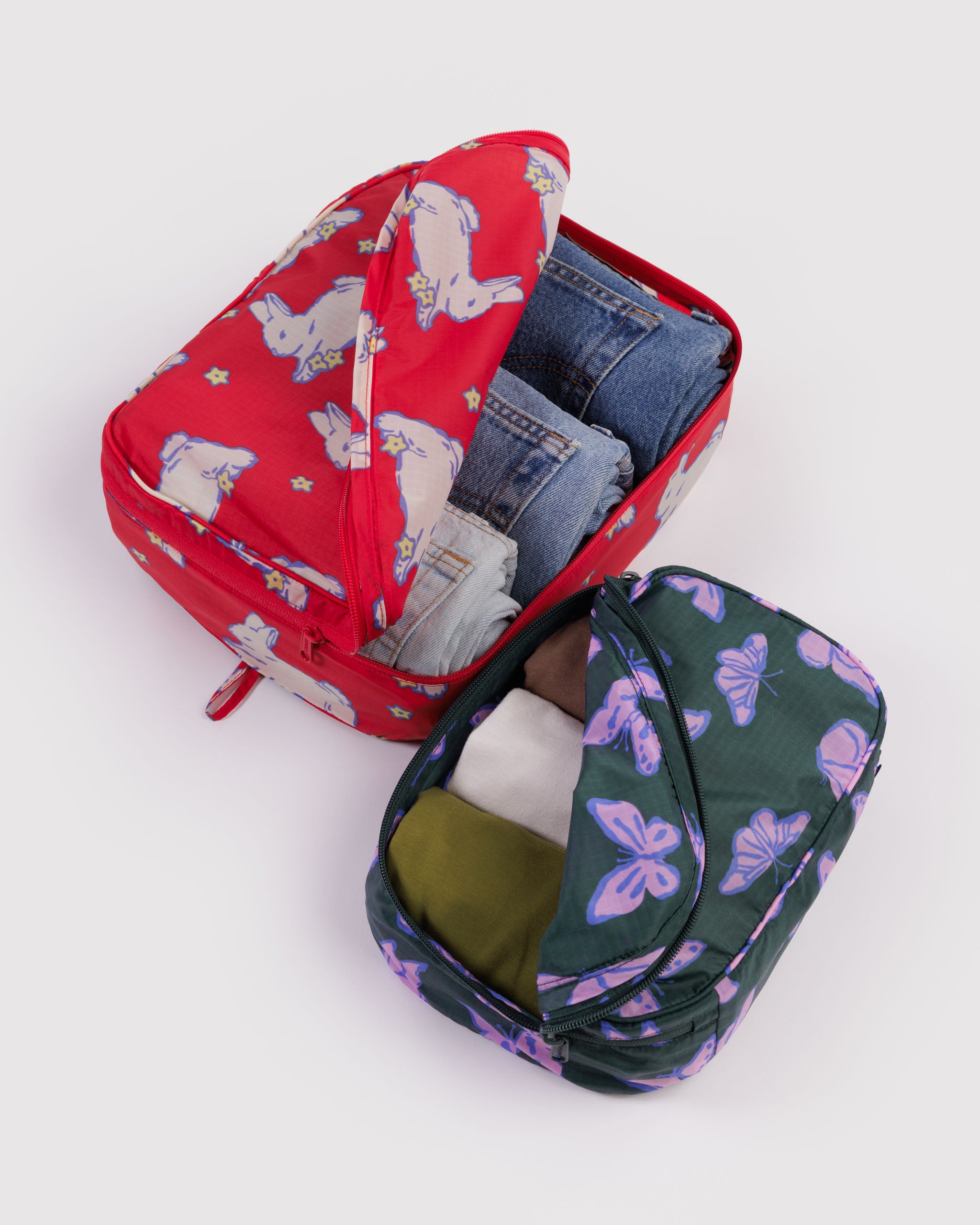 Set of two packing cubes a red medium size and a small green butterfly-patterned cube filled with clothes.