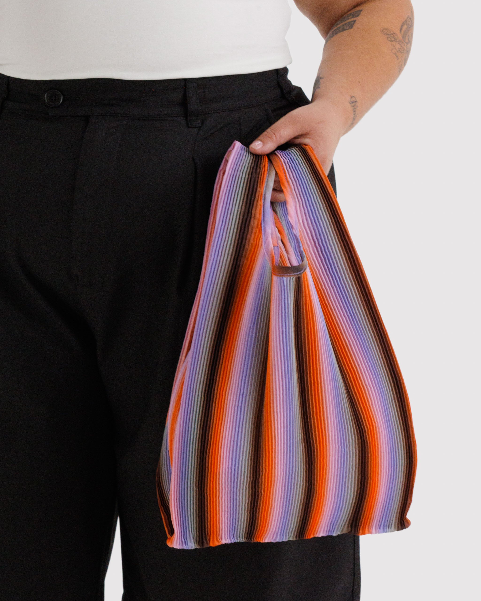 Person holding a colourful striped pleated tote bag in their hand.
