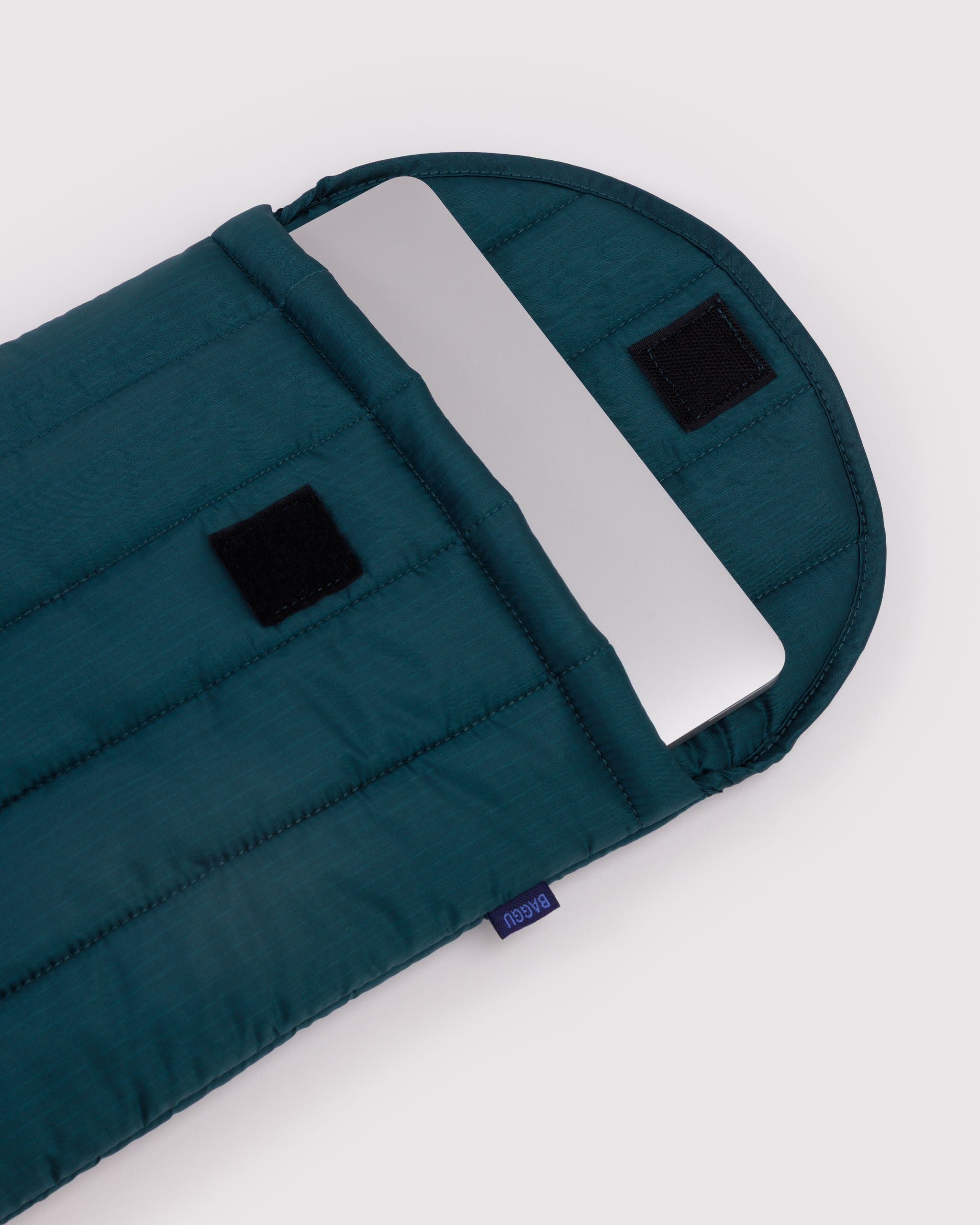 Teal quilted sleeve with velcro closure and silver laptop inside.