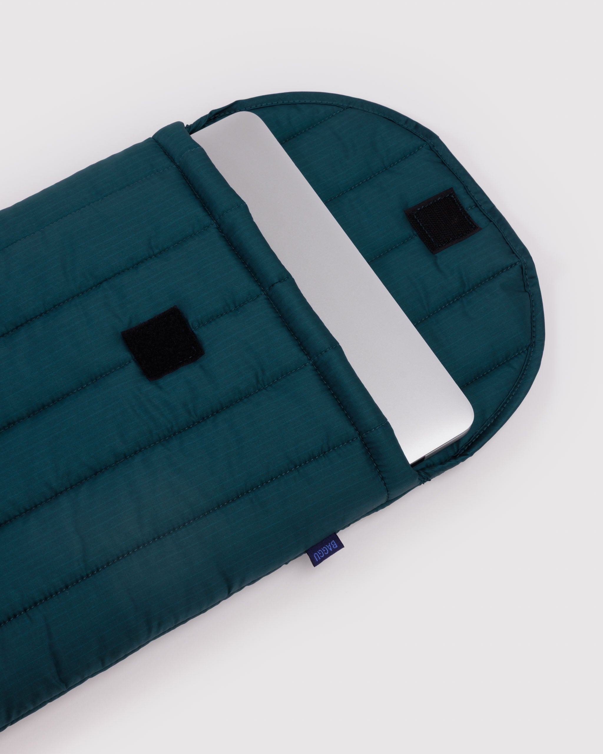 Green quilted bag with a silver laptop inside and a velcro closure.