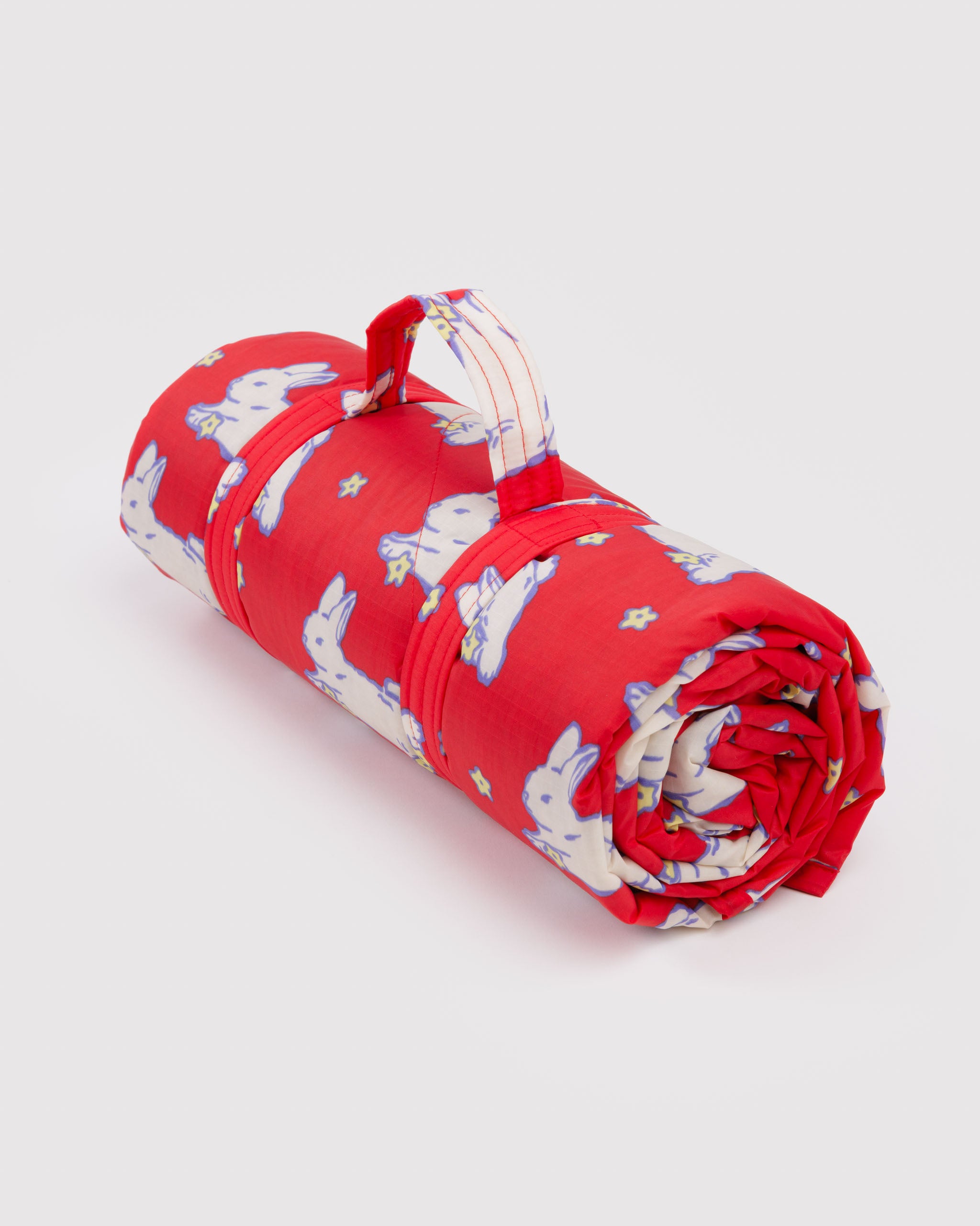 Rolled-up red puffy and quilted rug with white bunny pattern and carry handle.