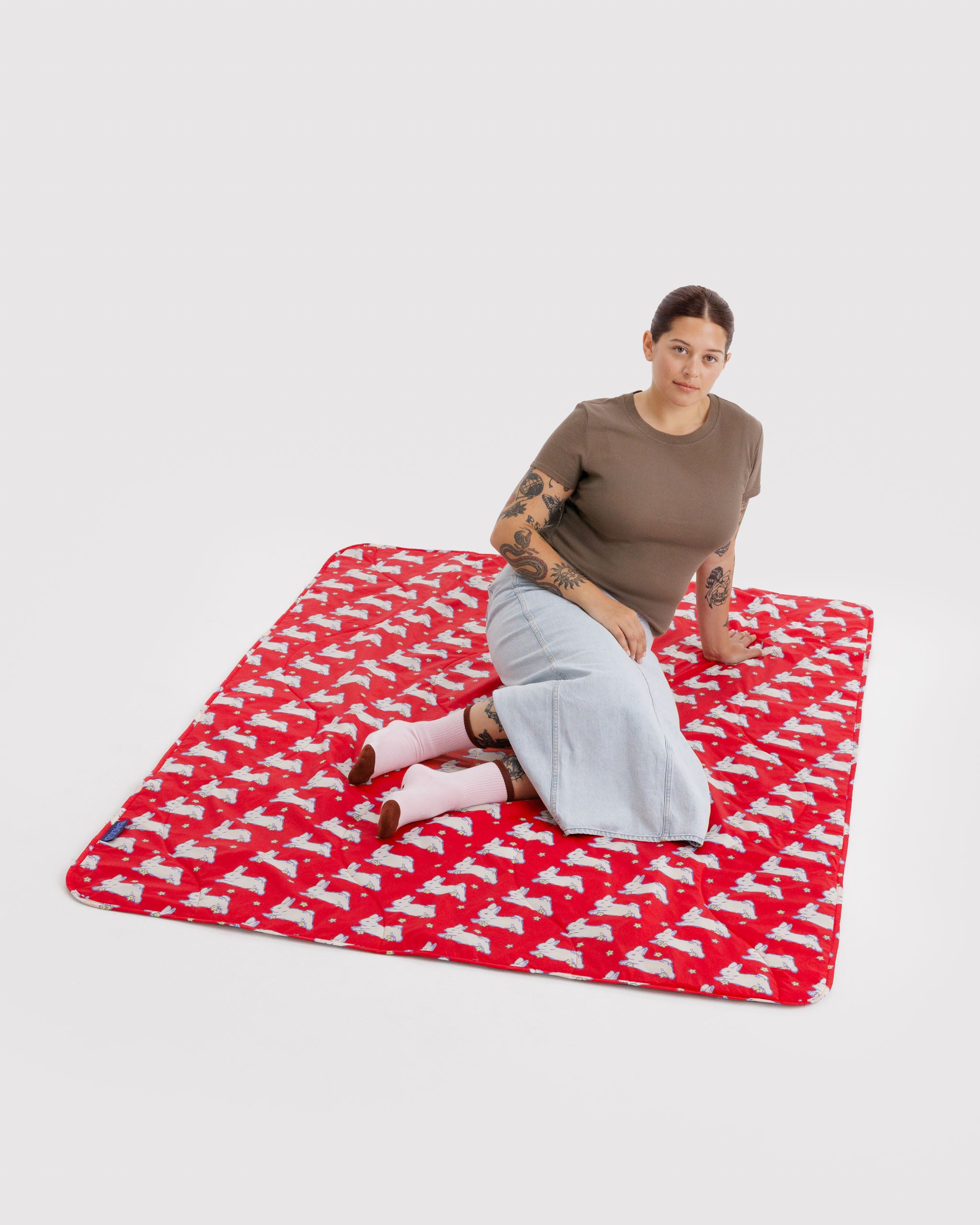 Person sitting on a red puffy and quilted mat with white bunnies and small yellow flowers.