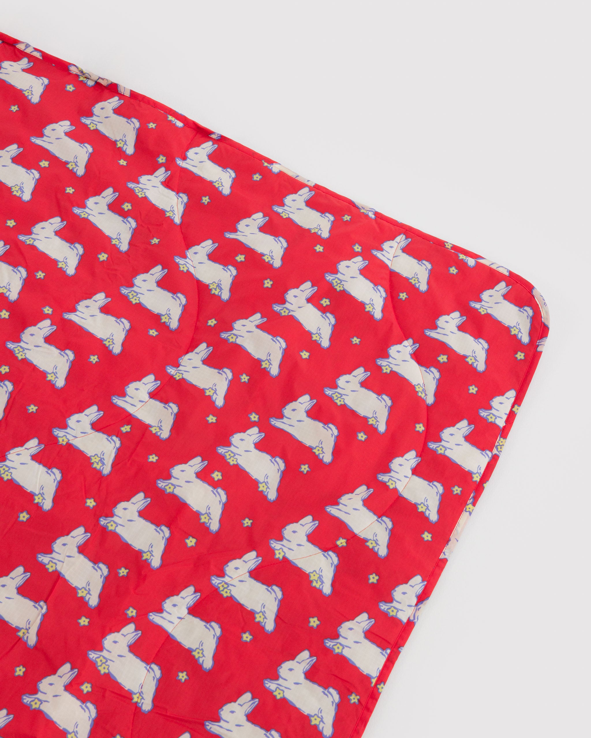 Red with white bunnies and small yellow flower patterned rectangular picnic rug.