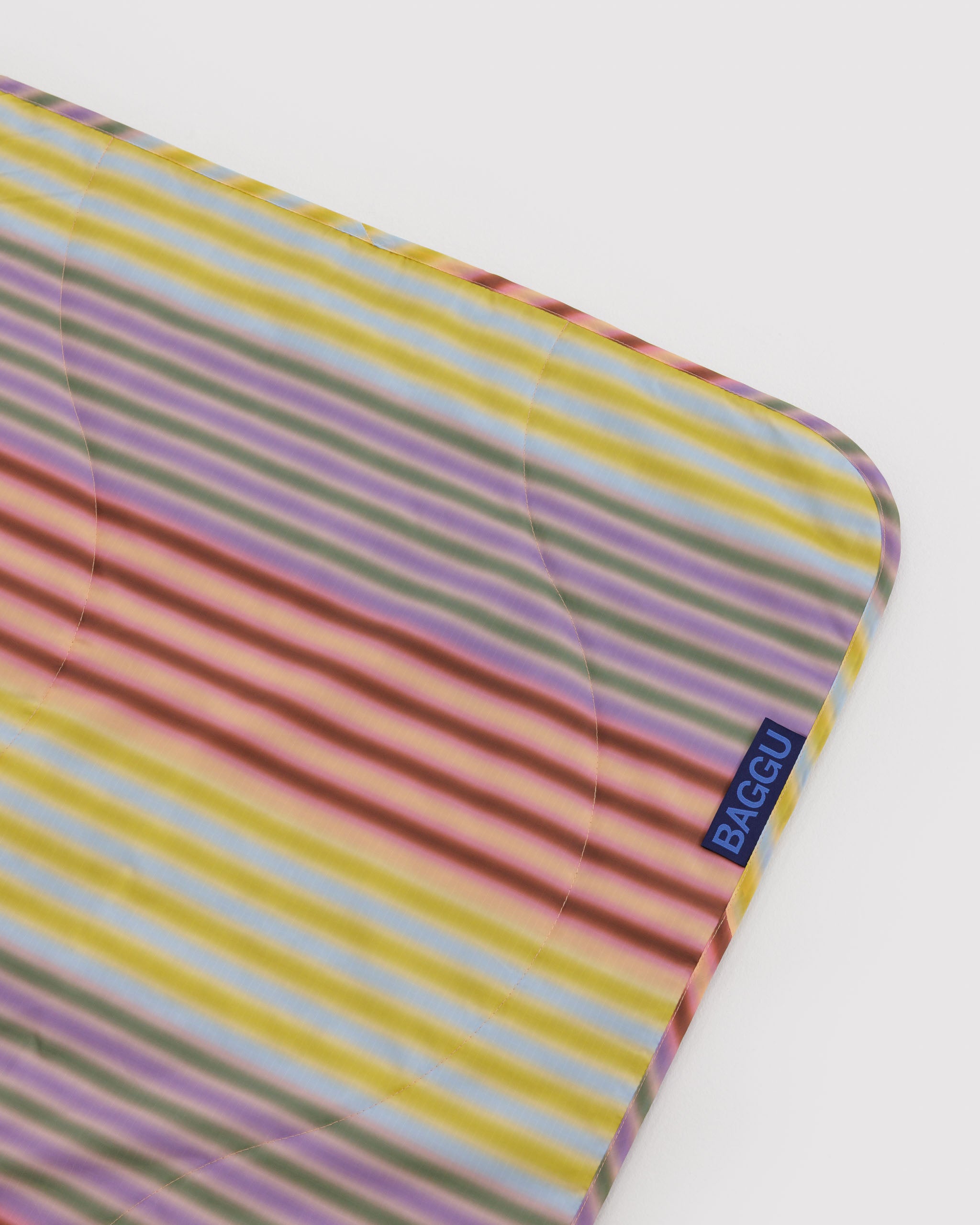 Corner edge of a colourful striped blanket with 'BAGGU' brand logo.