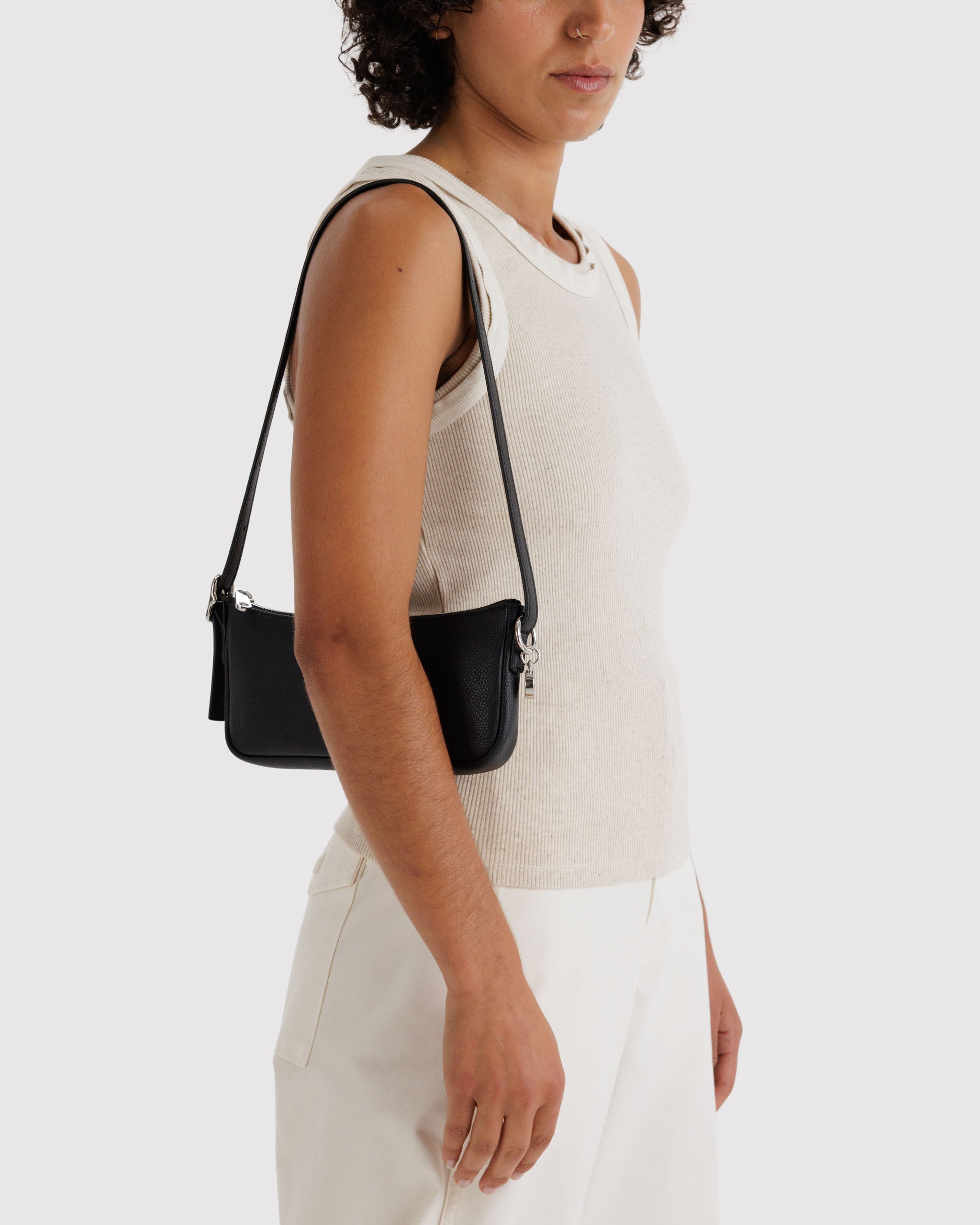 Person wearing a white sleeveless top and carrying a black leather handbag with an adjustable strap over shoulder.