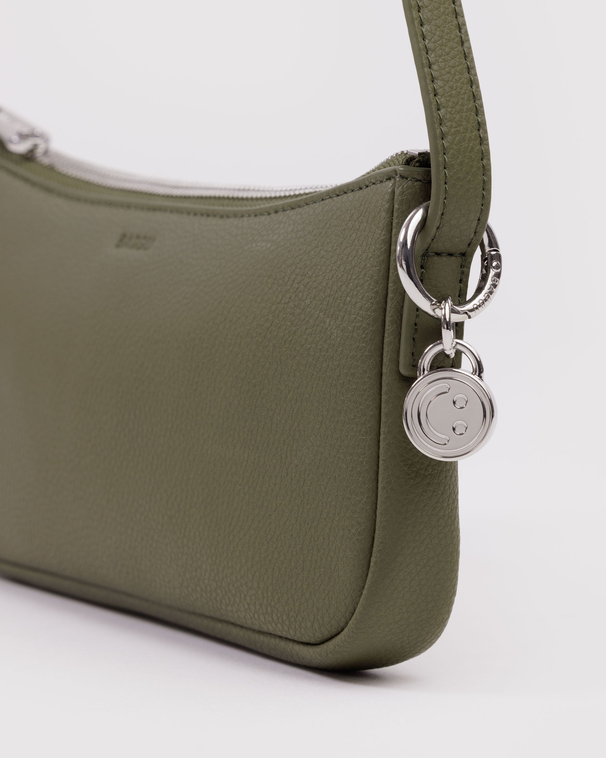 Green leather handbag with a metal silver smiley face bag charm attached to shoulder strap by a BAGGU branded metal silver ring.