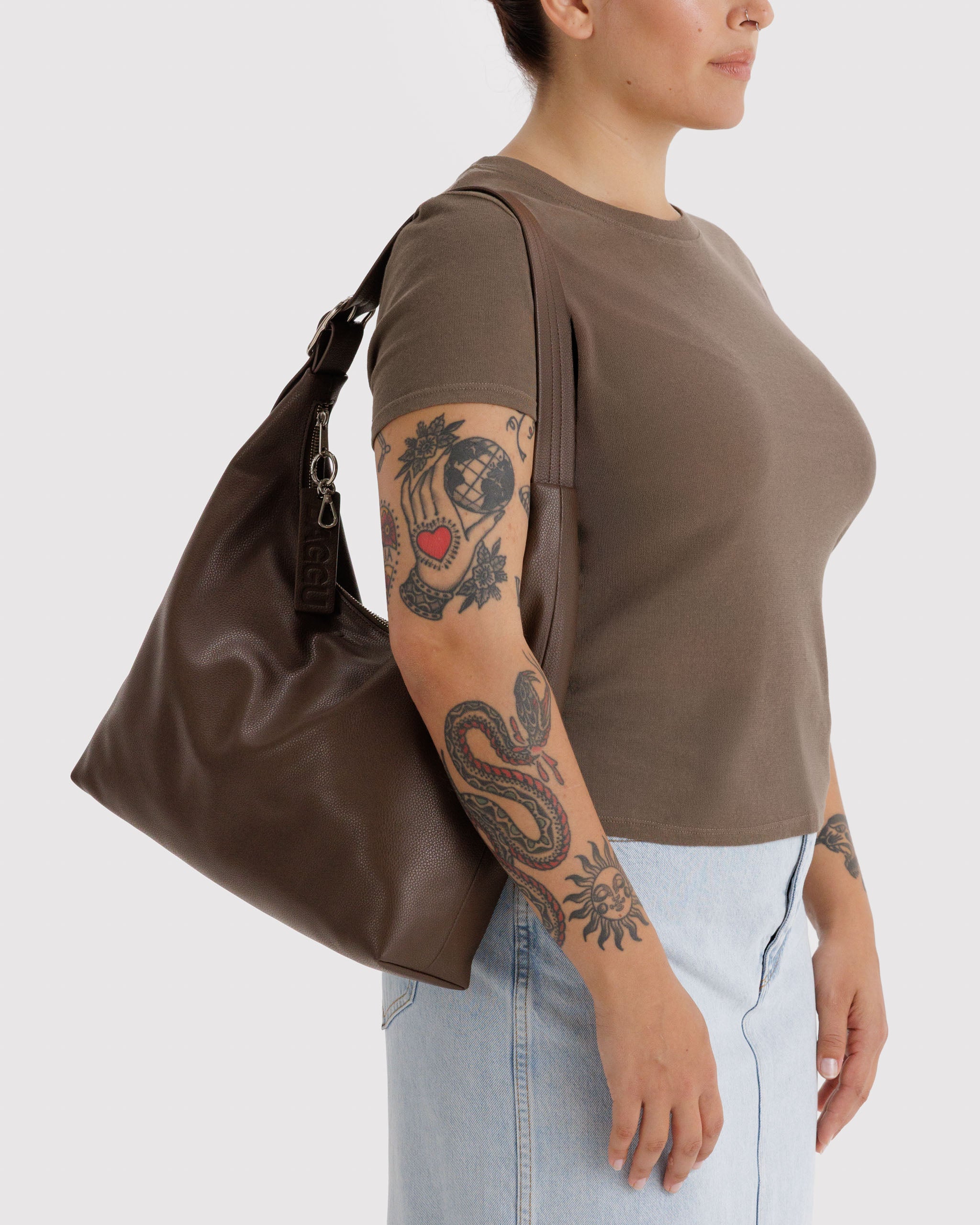 Woman wearing a brown top and carrying a brown leather bag on shoulder.
