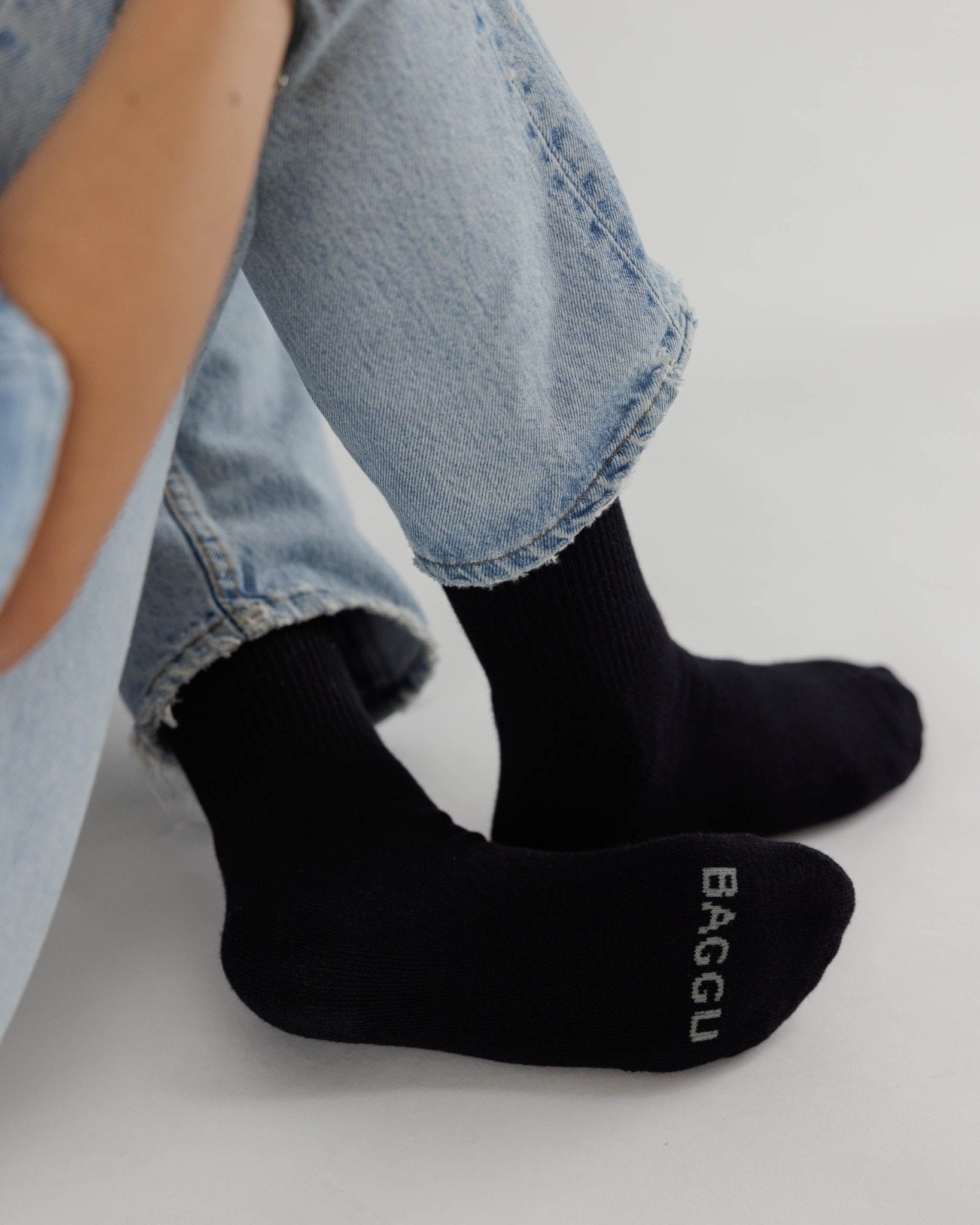 Person in jeans wearing black ribbed socks with 'BAGGU' branding