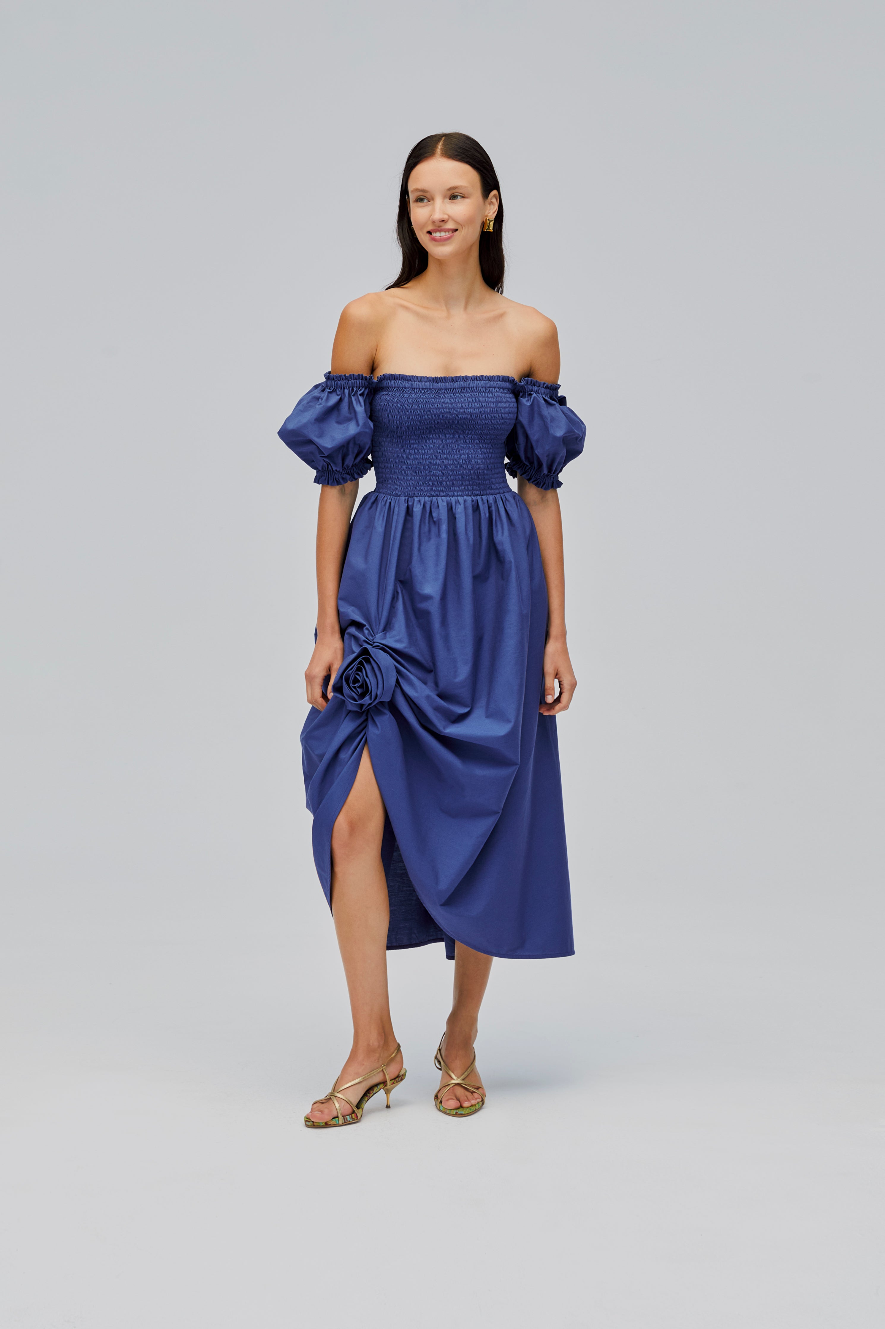 woman-wearing-navy-shirred-bodice-dress-with-short-sleeves-off-the-shoulder-showing-rose-detail-above-front-split