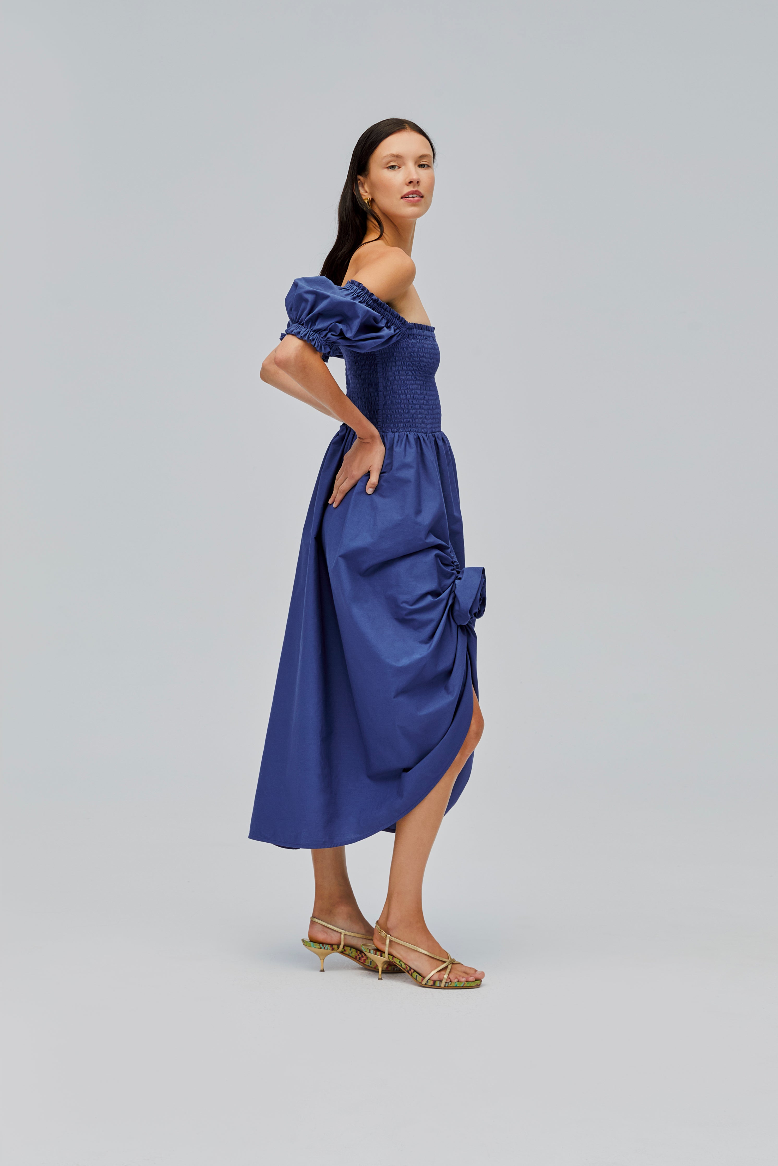 side-of-woman-wearing-navy-shirred-bodice-dress-with-short-sleeves-off-the-shoulder-with-front-split