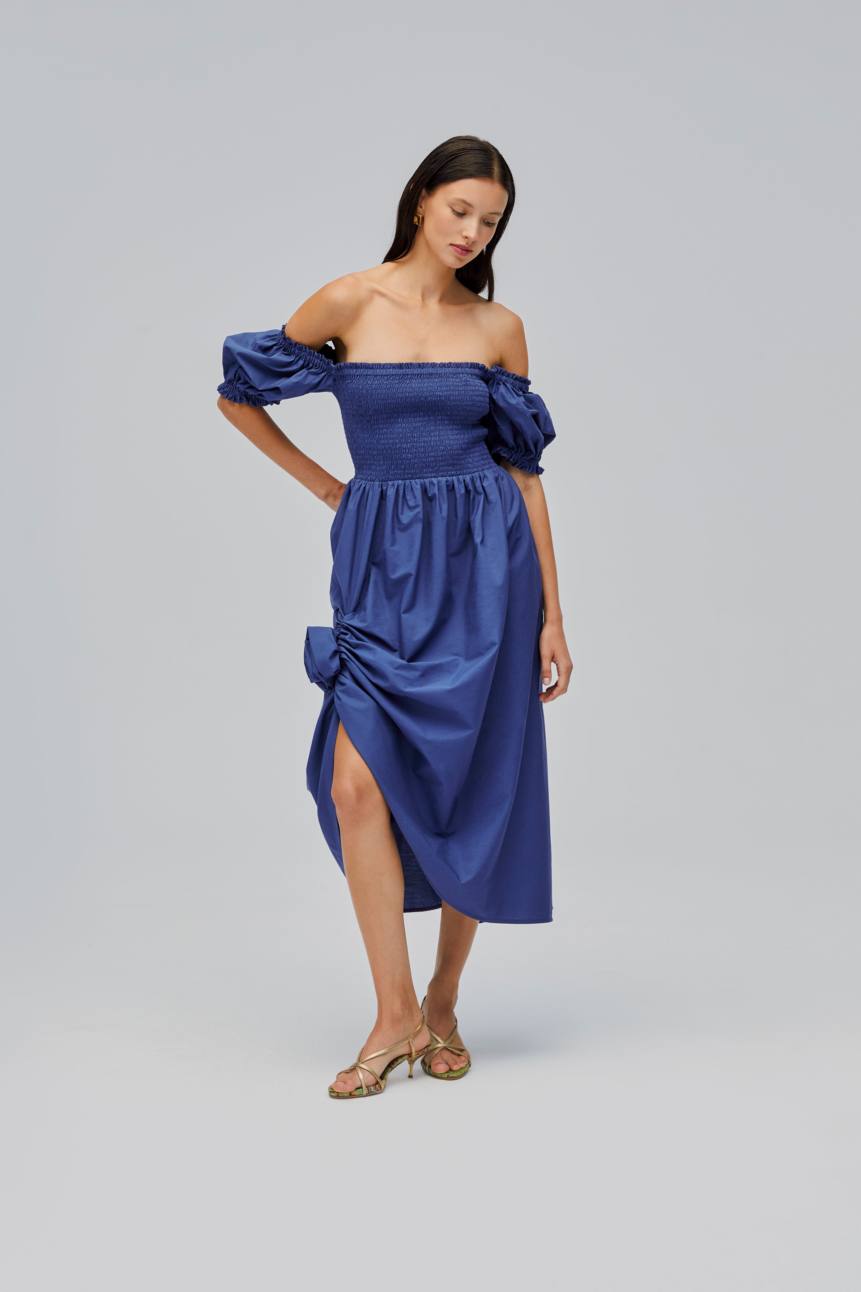 woman-wearing-navy-shirred-bodice-dress-with-short-puff-sleeves-off-the-shoulder-and-rose-detail-above-front-split