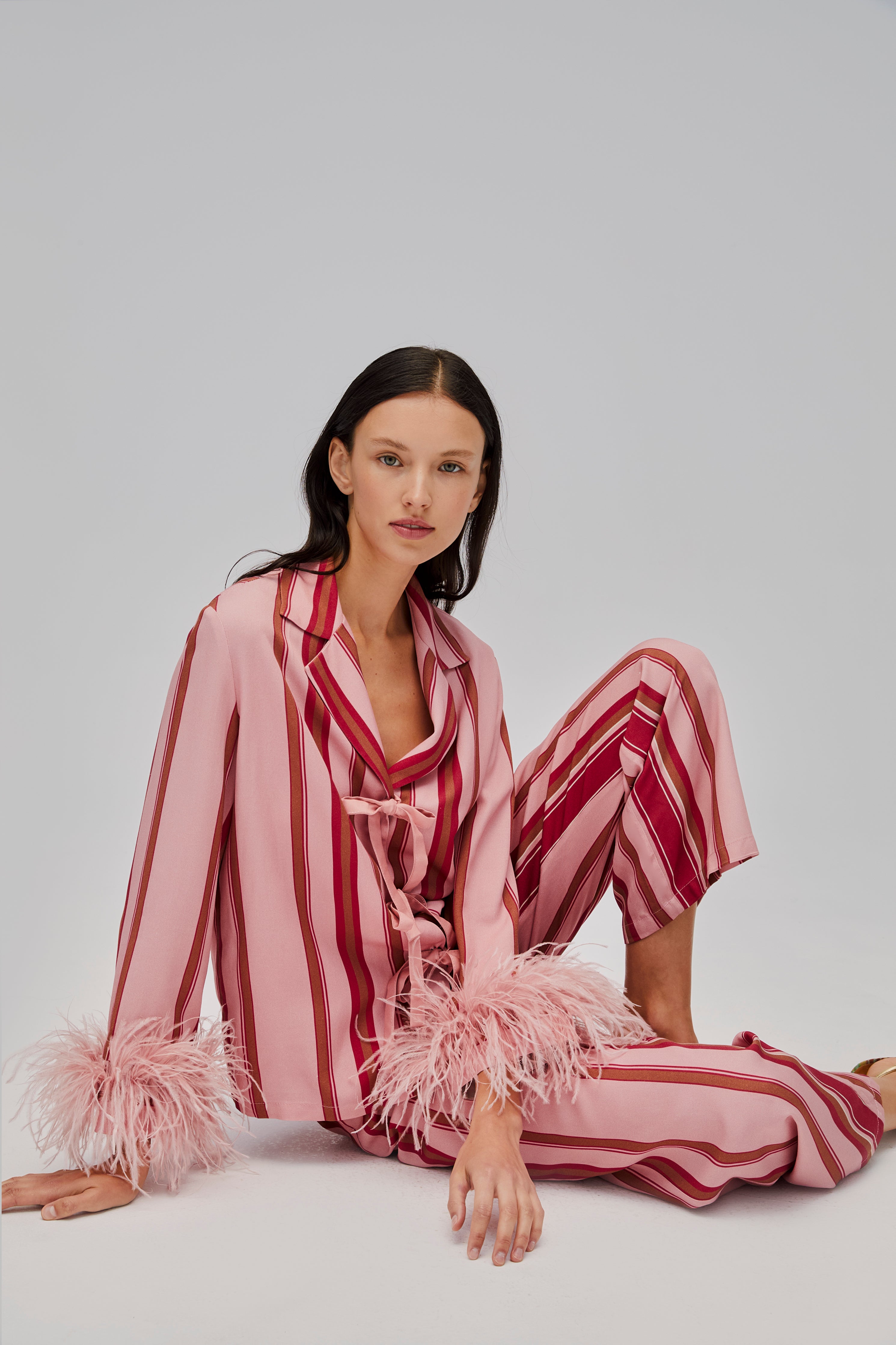 woman-sitting-on-floor-wearing-red-and-pink-striped-long-sleeve-shirt-with-feather-cuffs-and-tie-bow-closures-long-pants