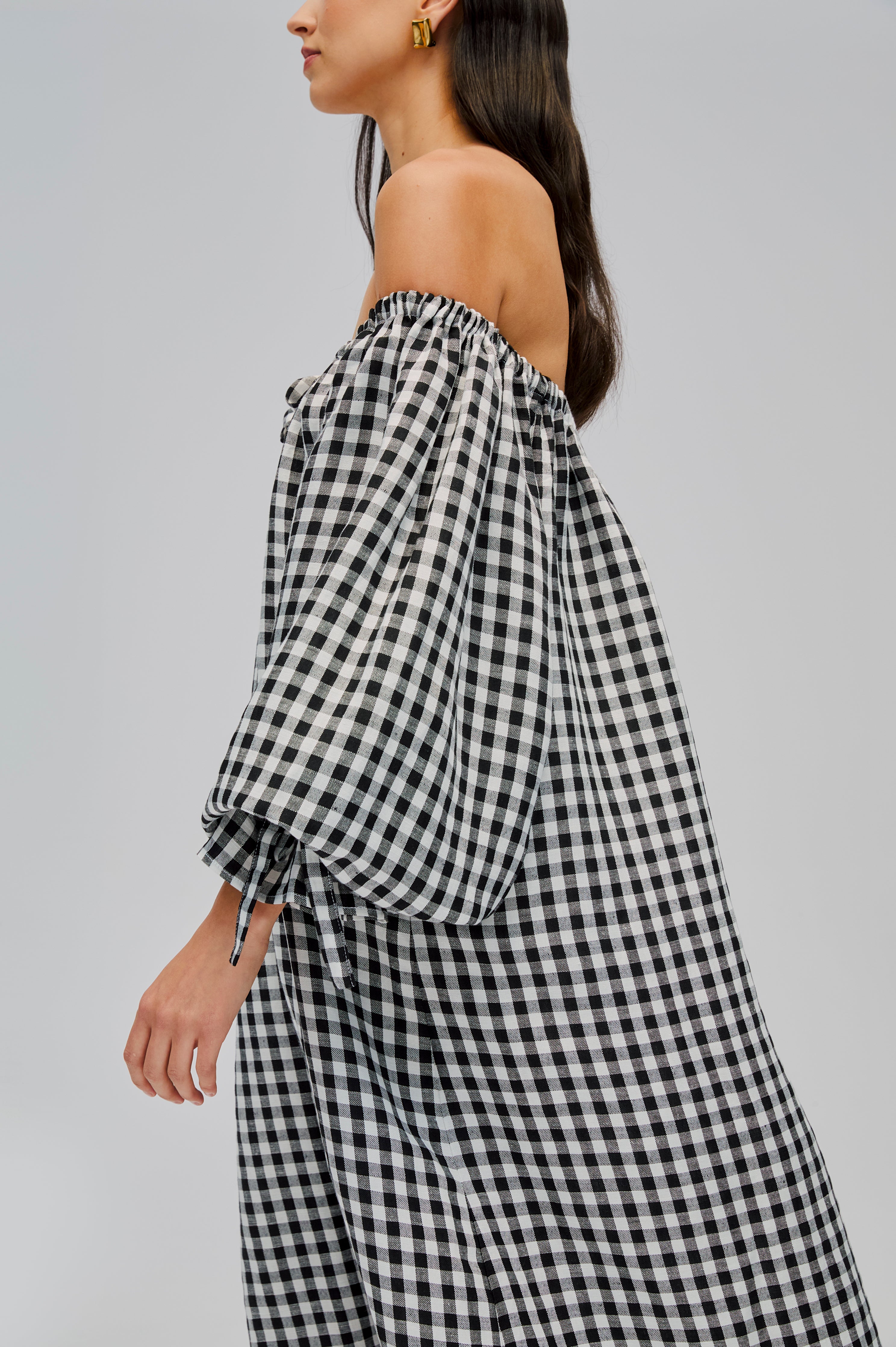 side-of-woman-wearing-black-gingham-dress-with-long-sleeves -tie-at-neckline-and-sleeve-cuffs-with-neckline-off-the-shoulder