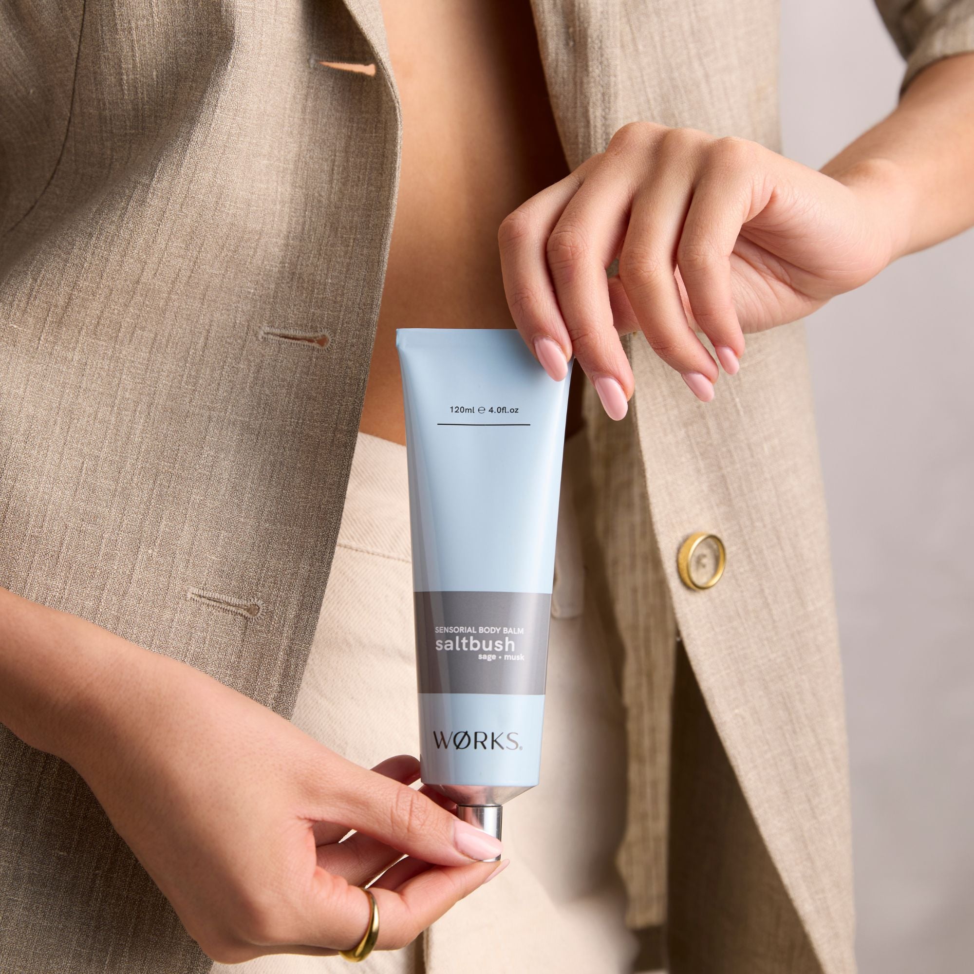 Person holding a blue aluminium tube of 'WORKS' skincare product in saltbush fragrance.