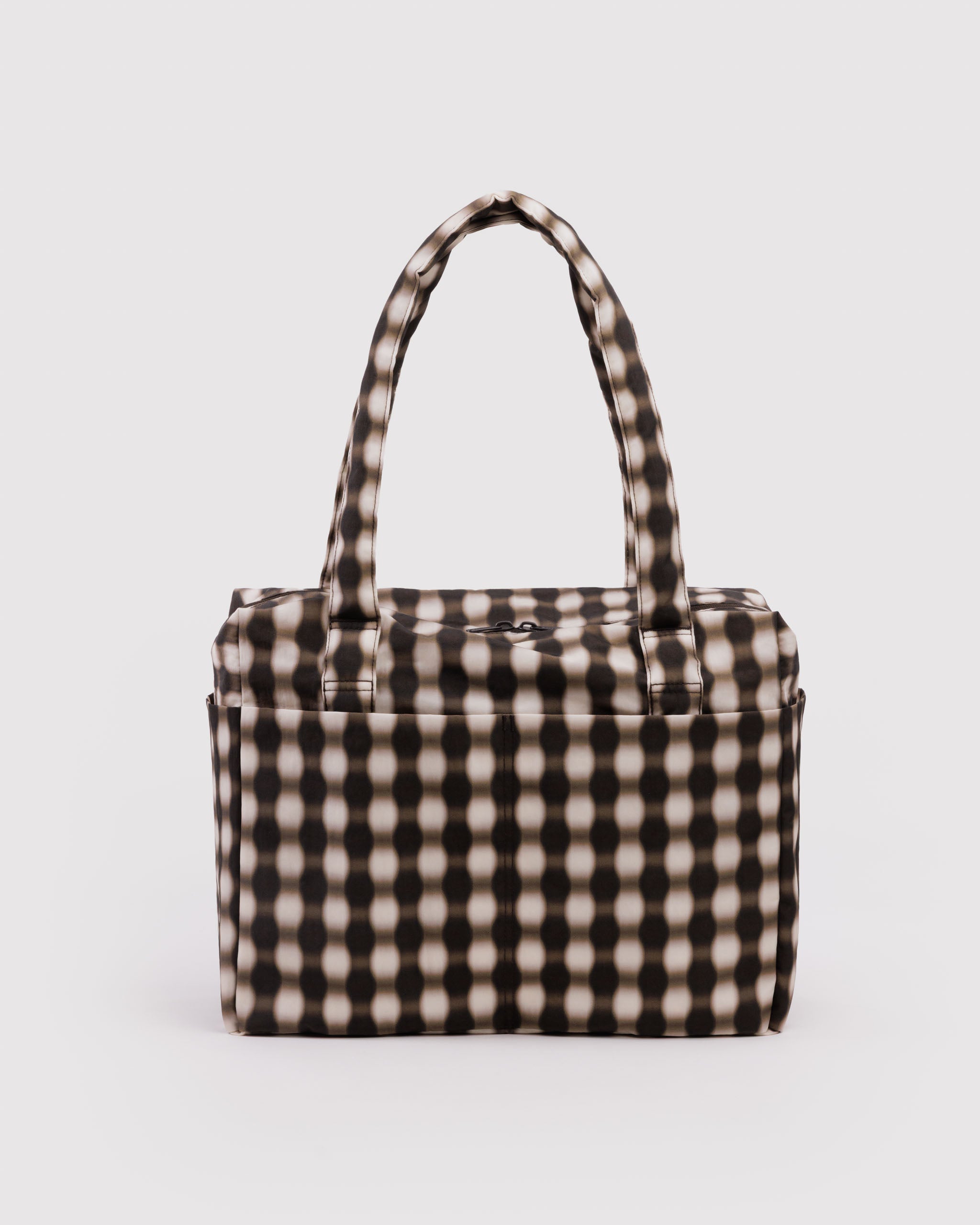 Checkered blurred brown and ecru gingham duffle bag with carry handles, top zip closure and exterior pockets.