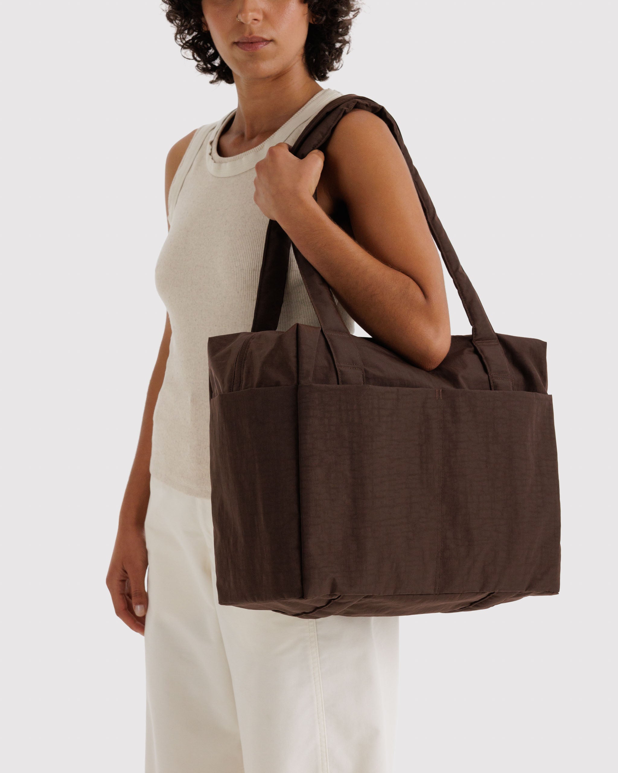 Woman holding a brown tote bag on shoulder by the double handles.