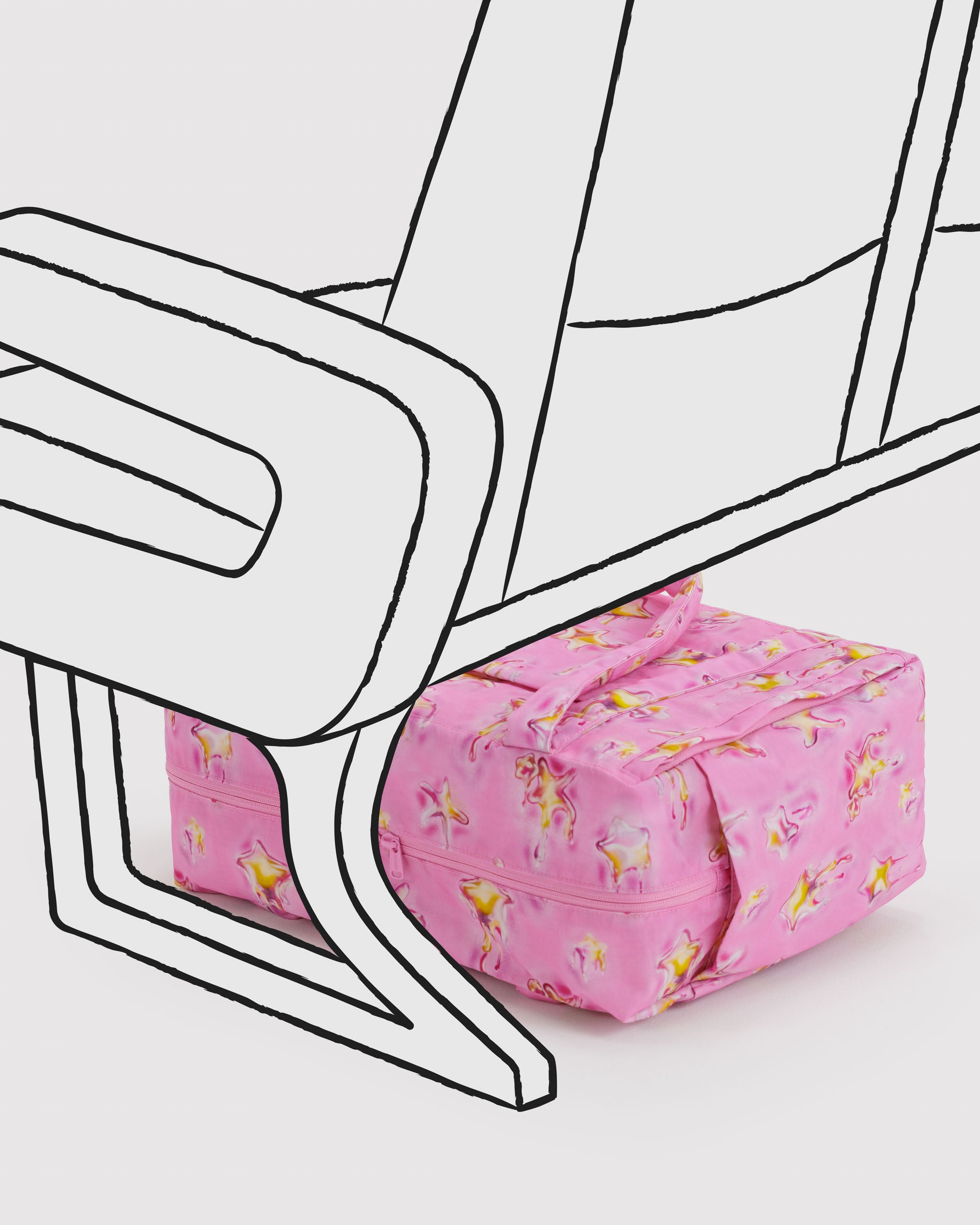 Pink and yellow star-patterned duffle bag lying on its side under a chair