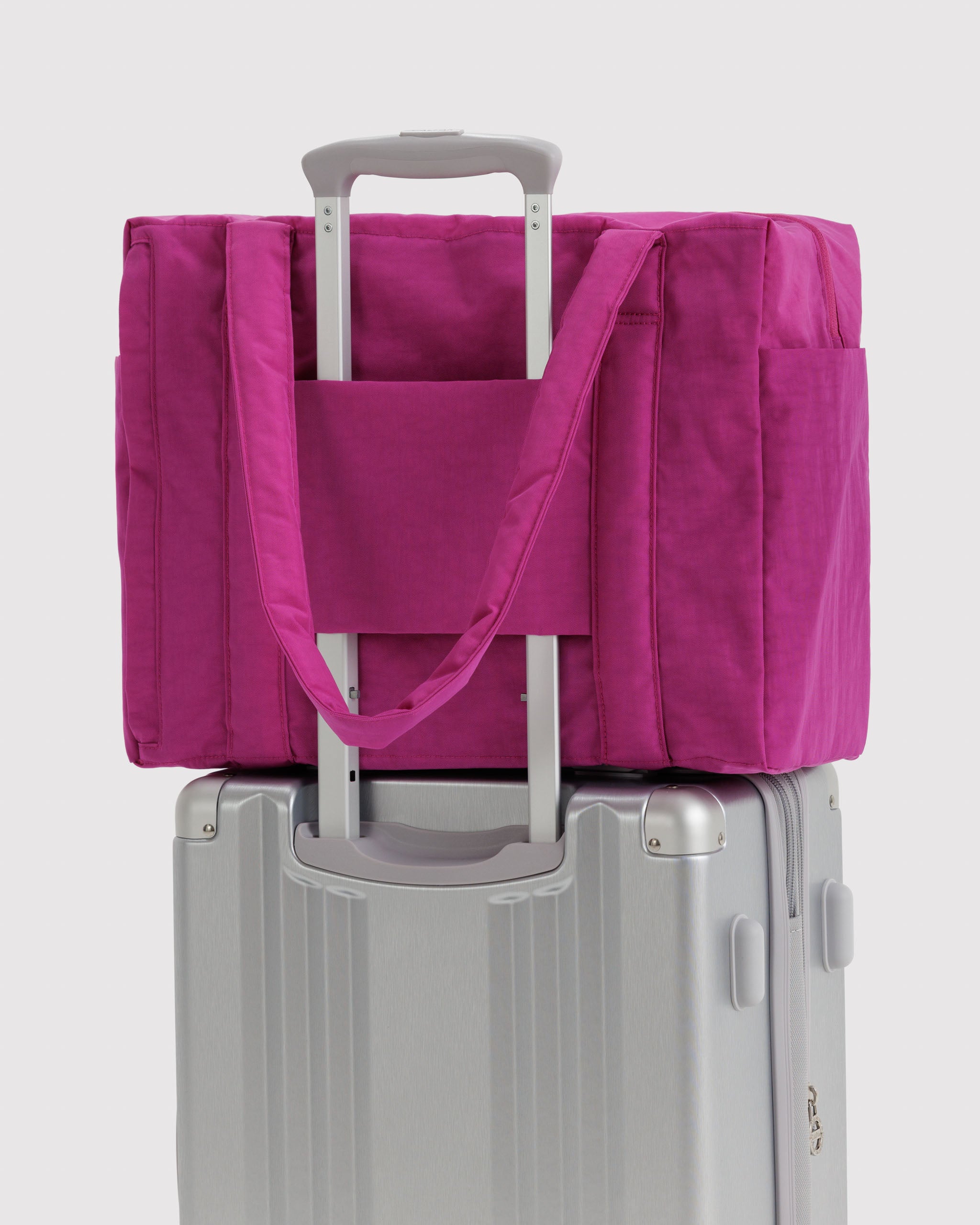 Vibrant pink tote bag sitting on a silver suitcase with trolley sleeve over handle.
