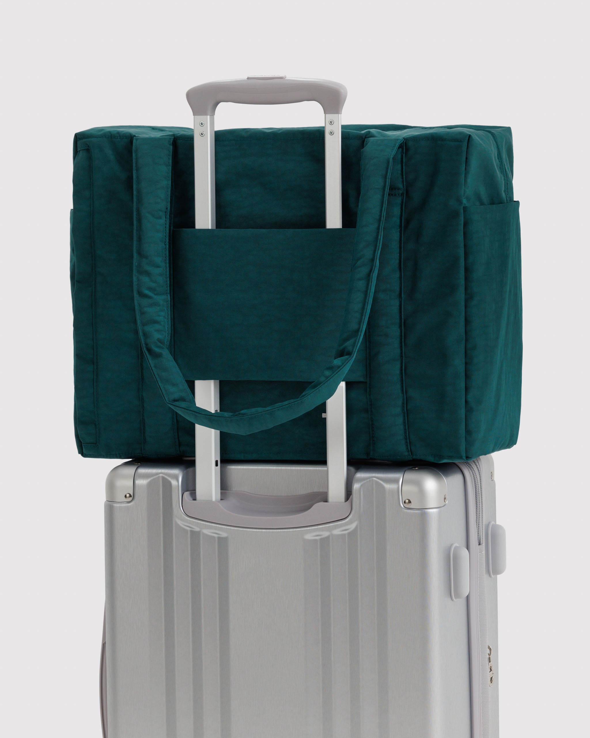 Green travel bag with handles on top of a silver suitcase with trolley sleeve over handle.