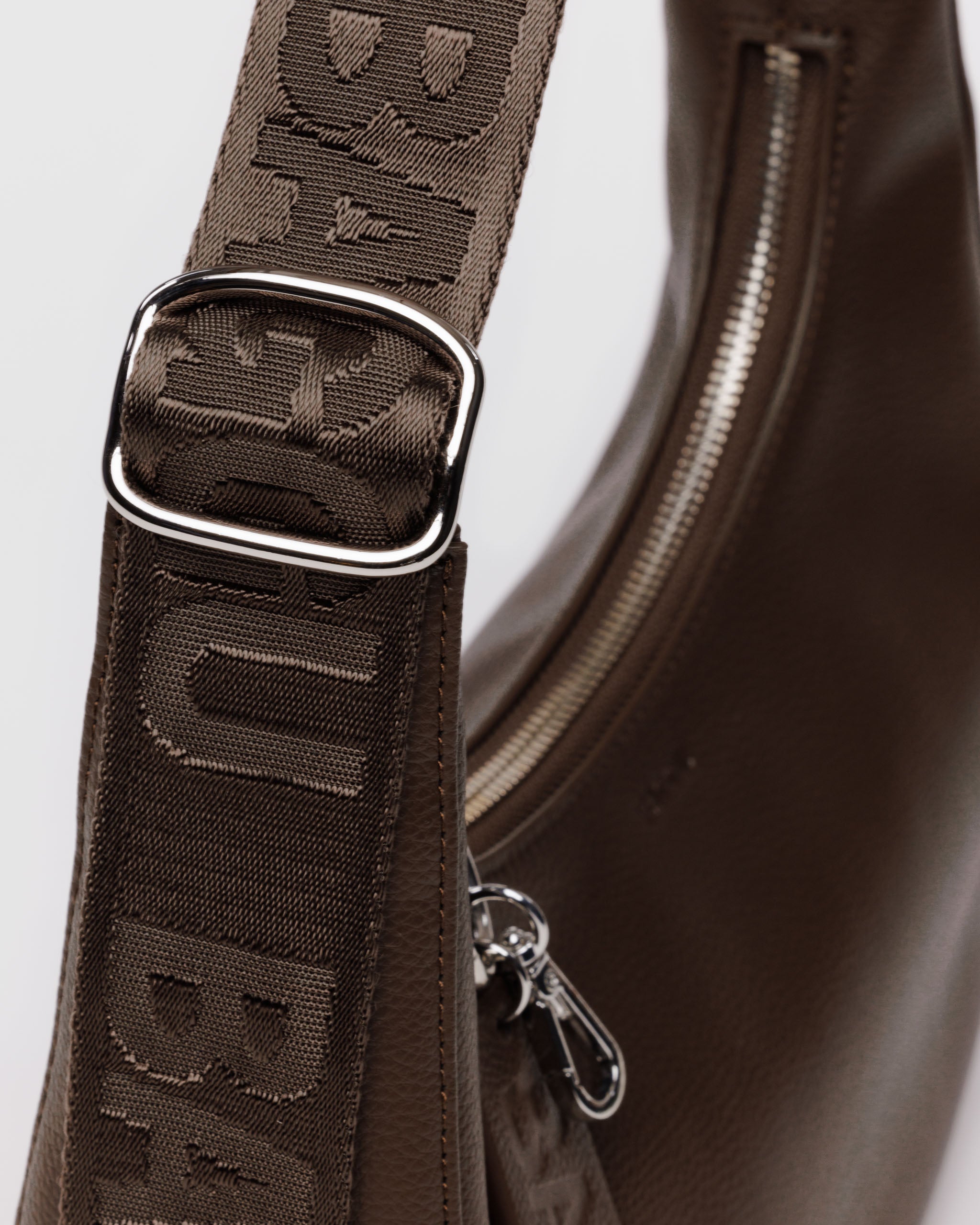 brown-recycled-leather-crescent-bag-logo-strap-showing-closeup-of-silver-hardware-buckle-on-strap-and-carabiner-on-zip
